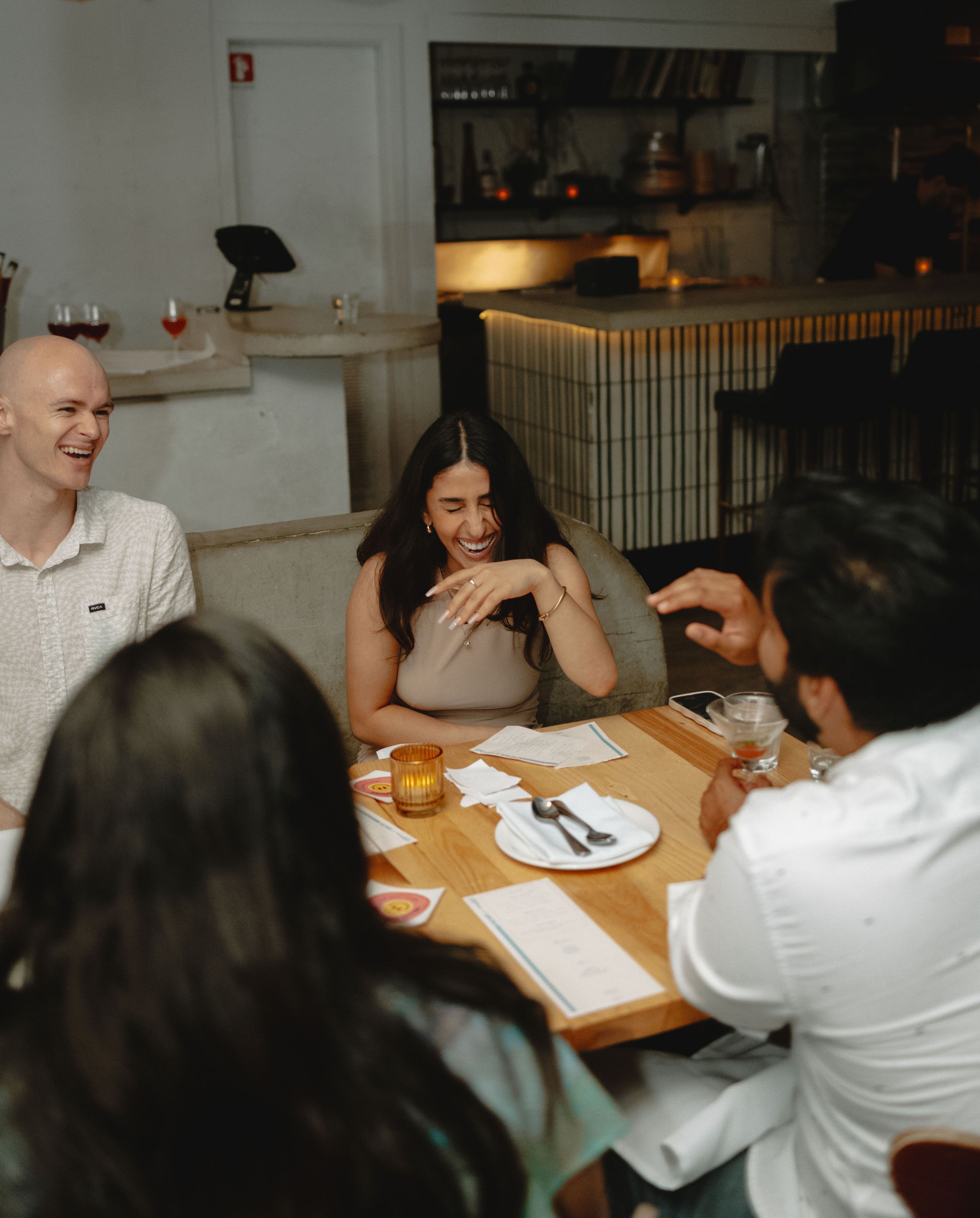 Four people chatting and laughing at a small restaurant table