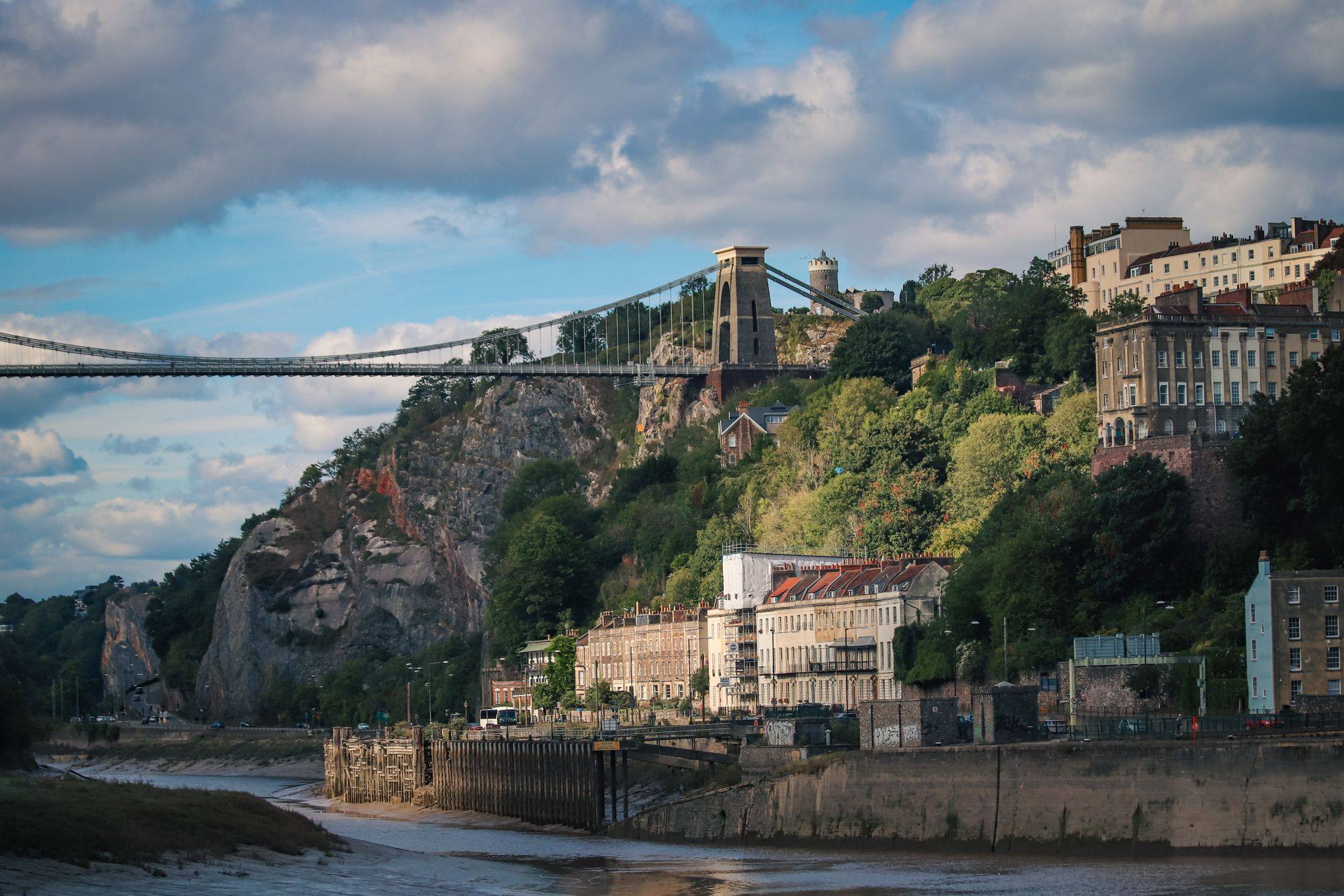 The Clifton Suspension Bridge crossing the Avon Gorge in Bristol, with the cliffside and houses below.