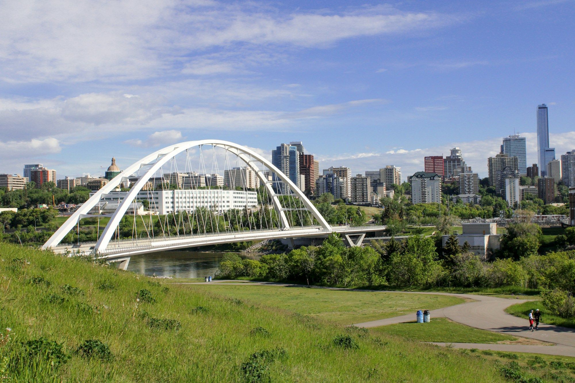 The Walterdale Bridge and the river valley in Edmonton, with walkers on the grass slope