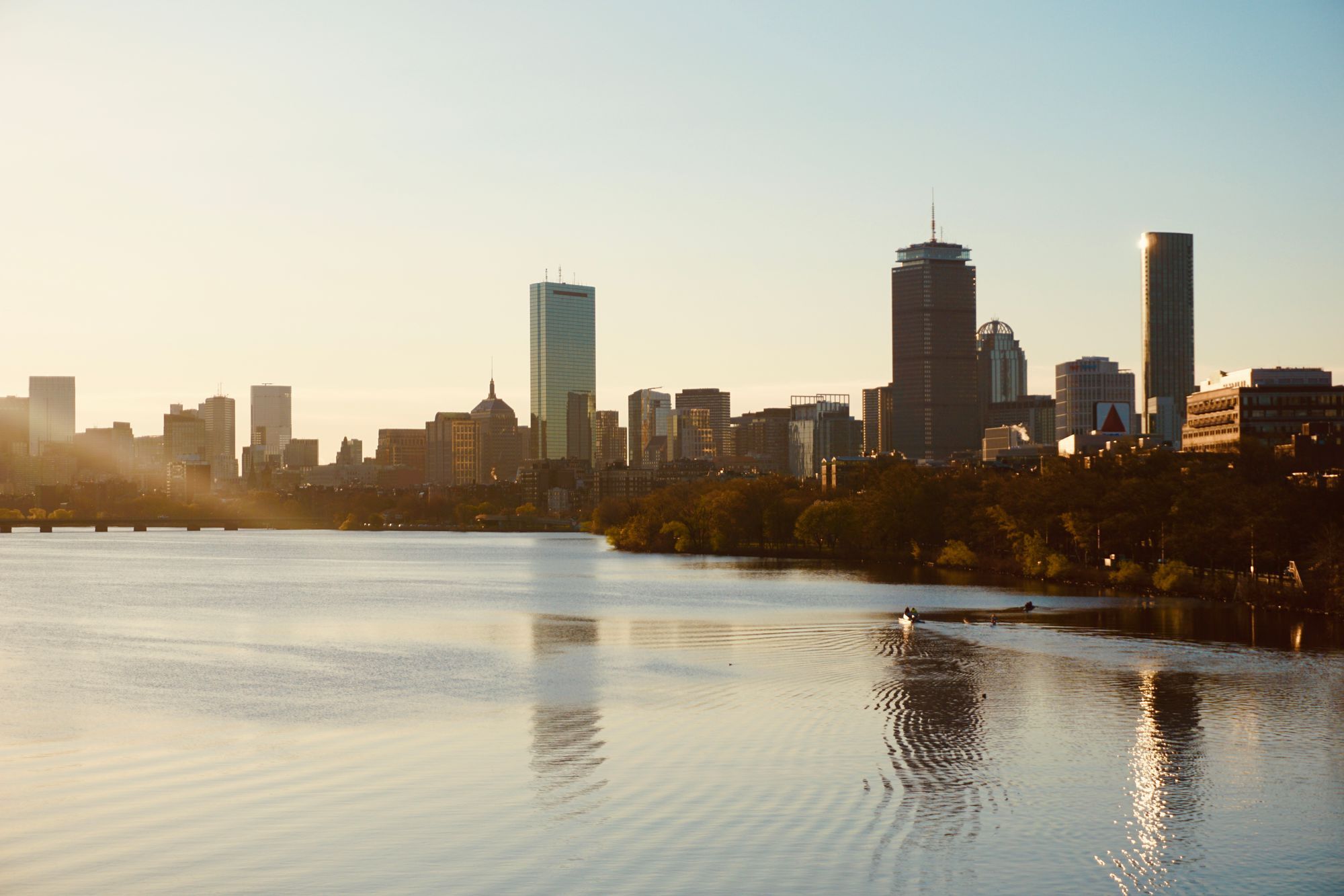 The Back Bay skyline of Boston, with the Hancock Tower and the Prudential Tower, seen across the Charles River at sunset.