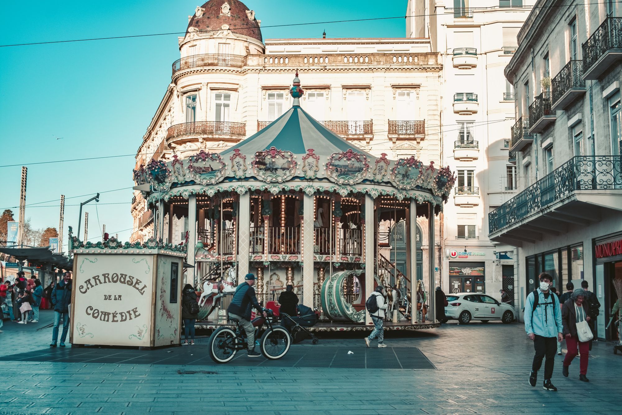 The carousel on the Place de la Comédie in Montpellier, with passers-by in front of the buildings.