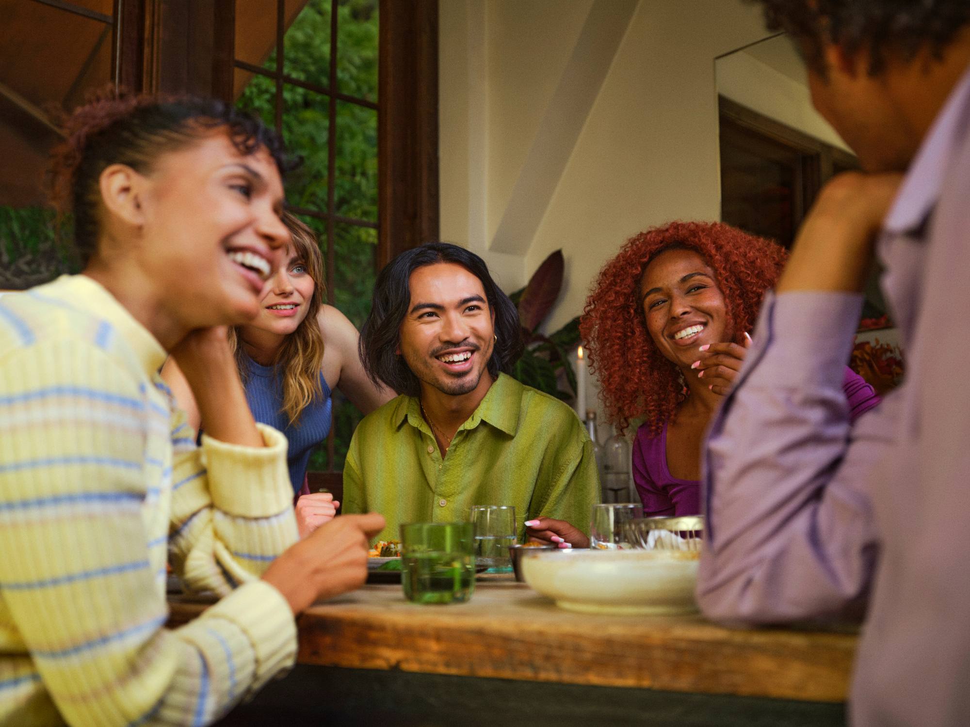 Cinco personas riéndose juntas alrededor de una mesa de madera en una cena de Timeleft