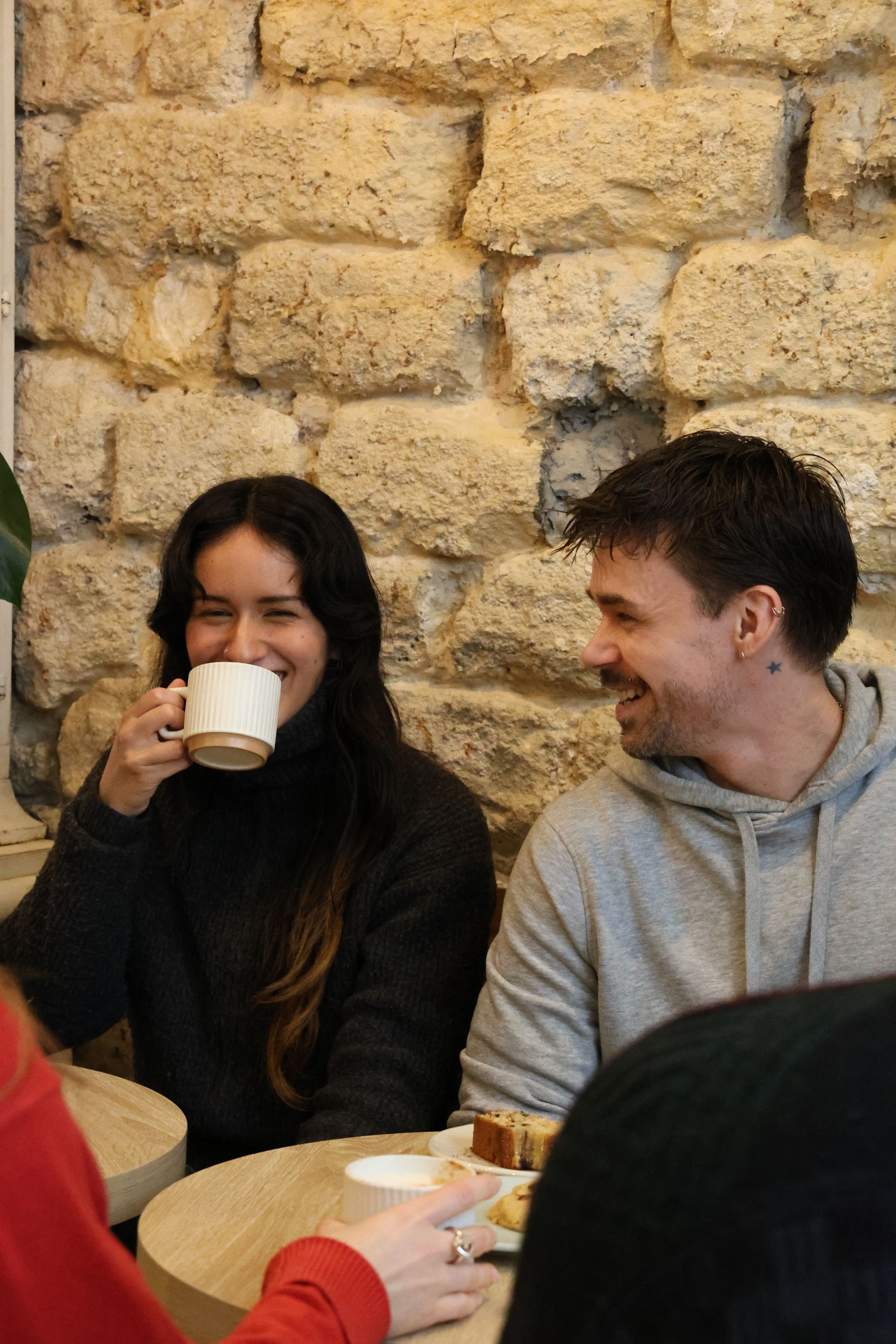 A woman sipping coffee next to a laughing man in a stone-walled café