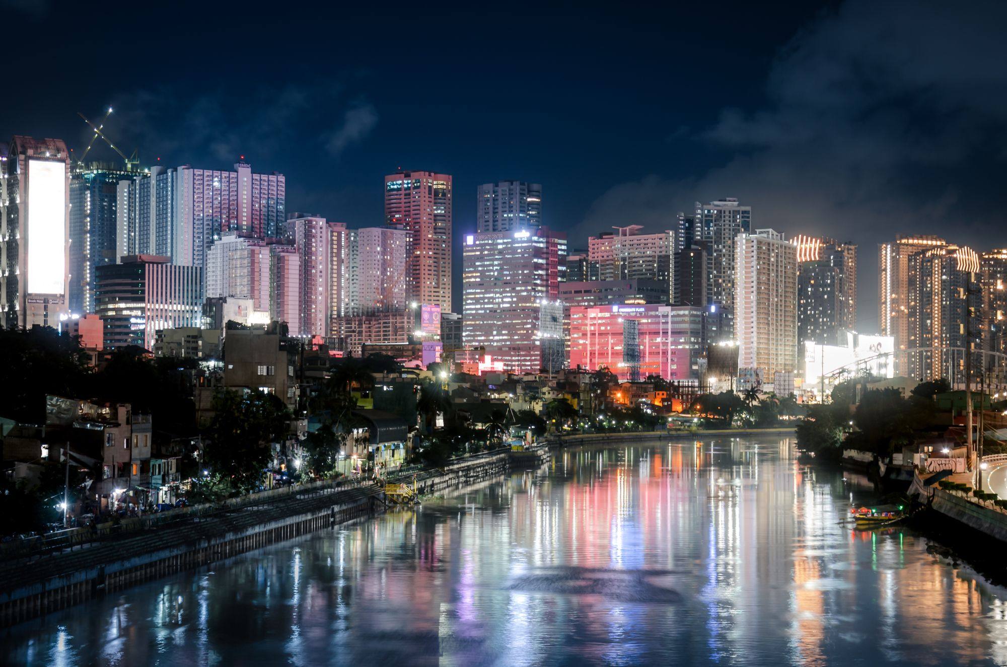 The illuminated skyline of Makati at night, reflected in the river in front.