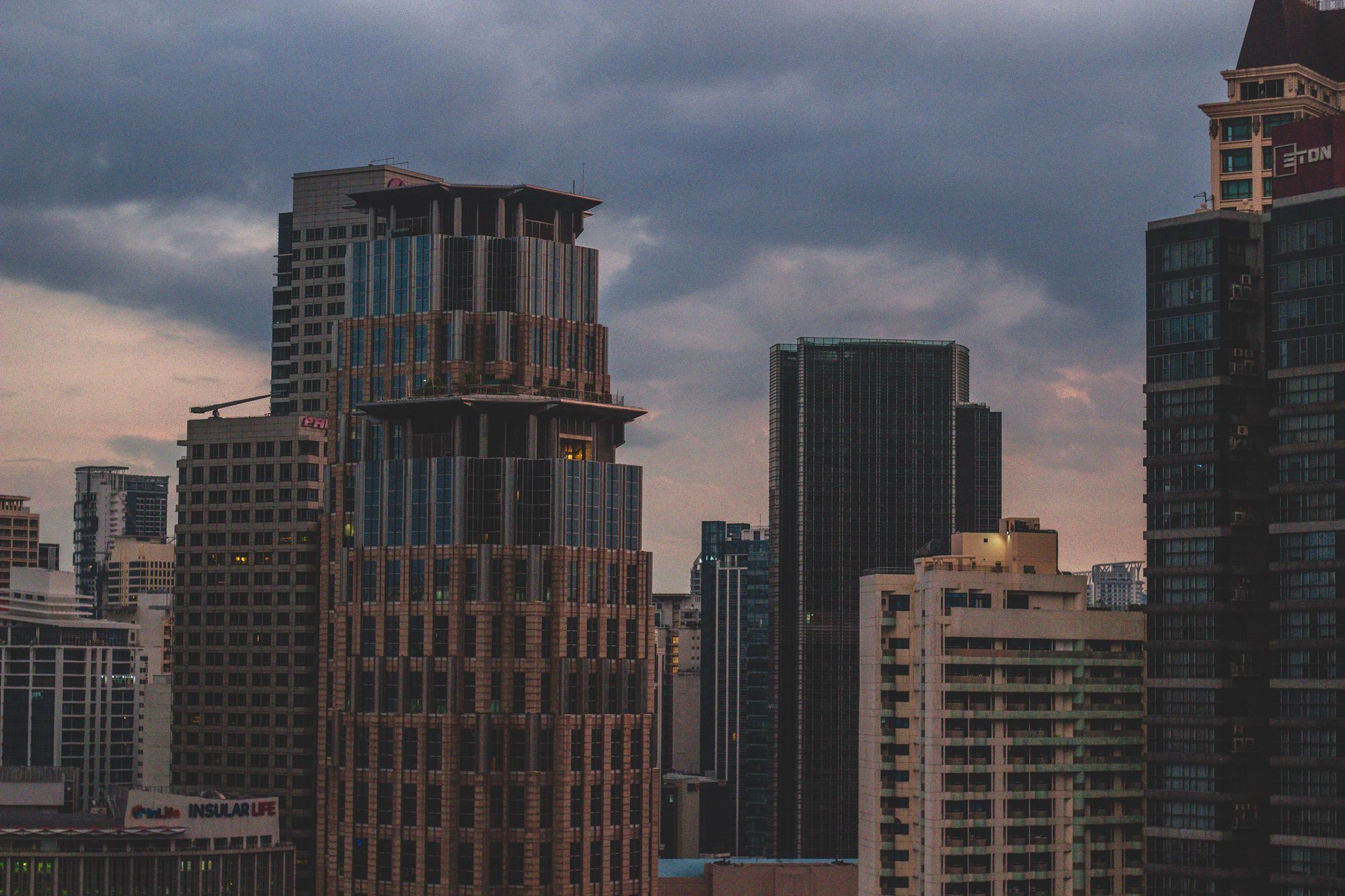 Tall towers in Makati at dusk under a cloudy sky.