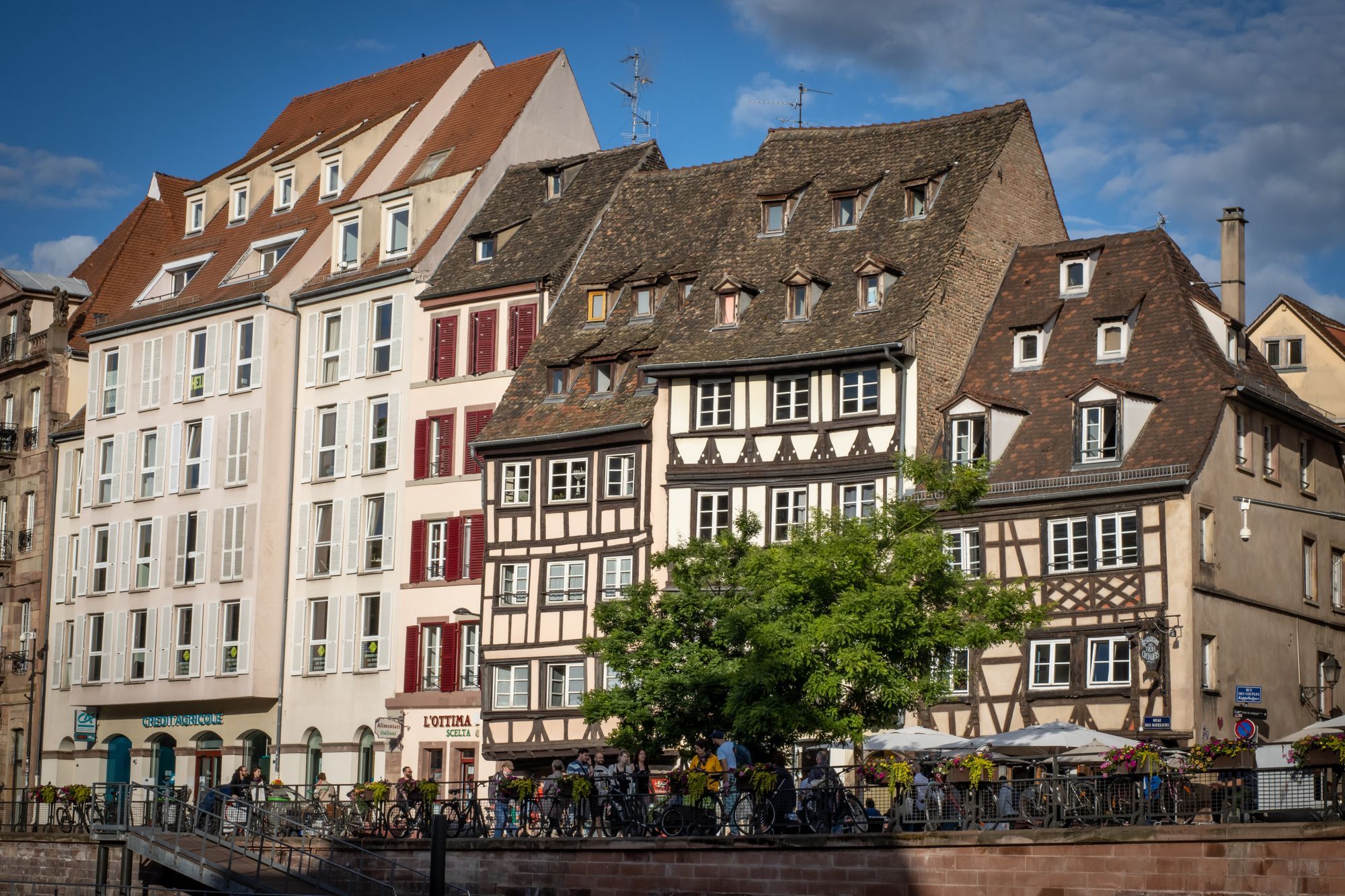 Half-timbered houses and townhouses along a canal quay in the old town of Strasbourg, with people at the water's edge.