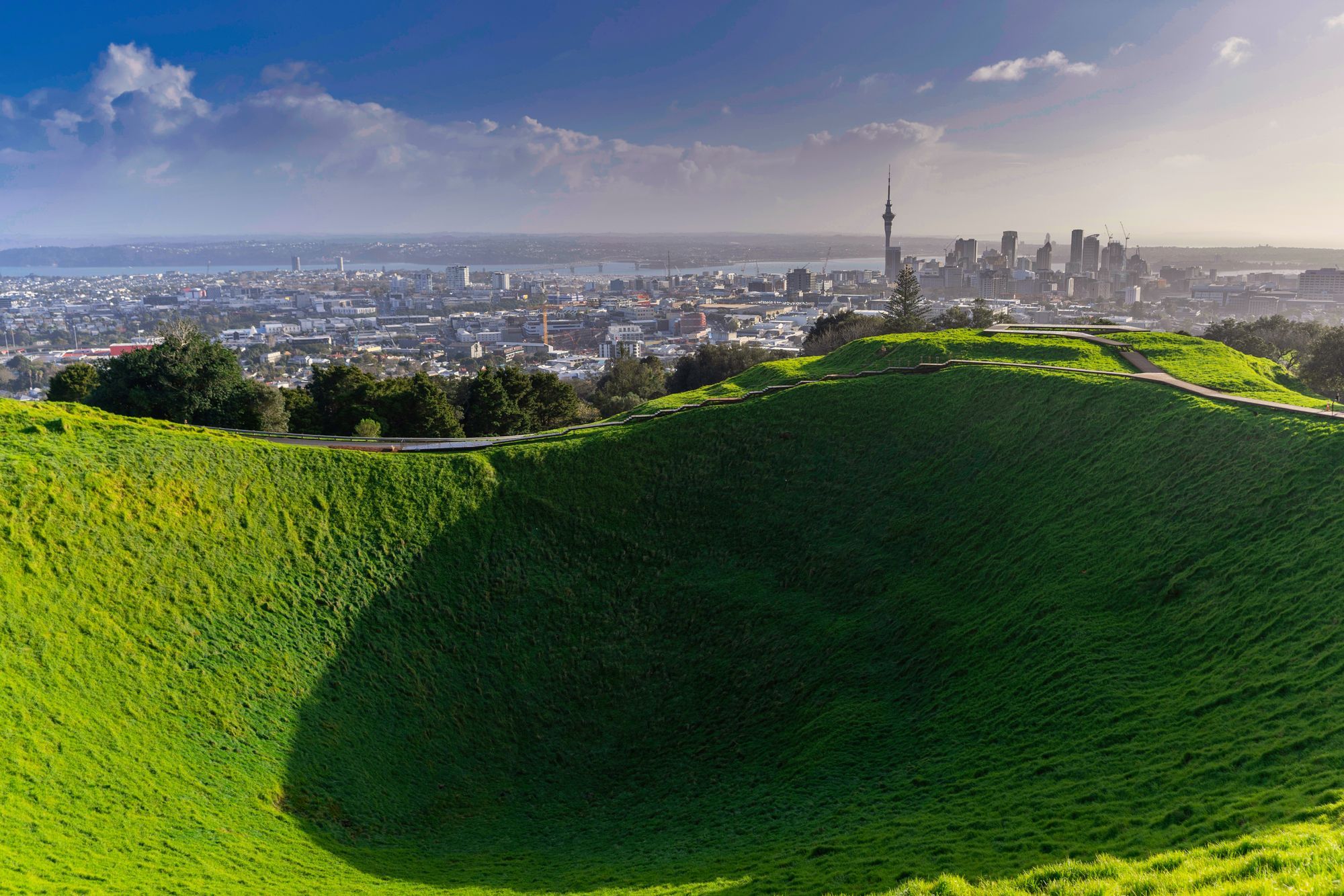 The grassy Mount Eden crater in Auckland, with the city skyline and the Sky Tower in the distance.