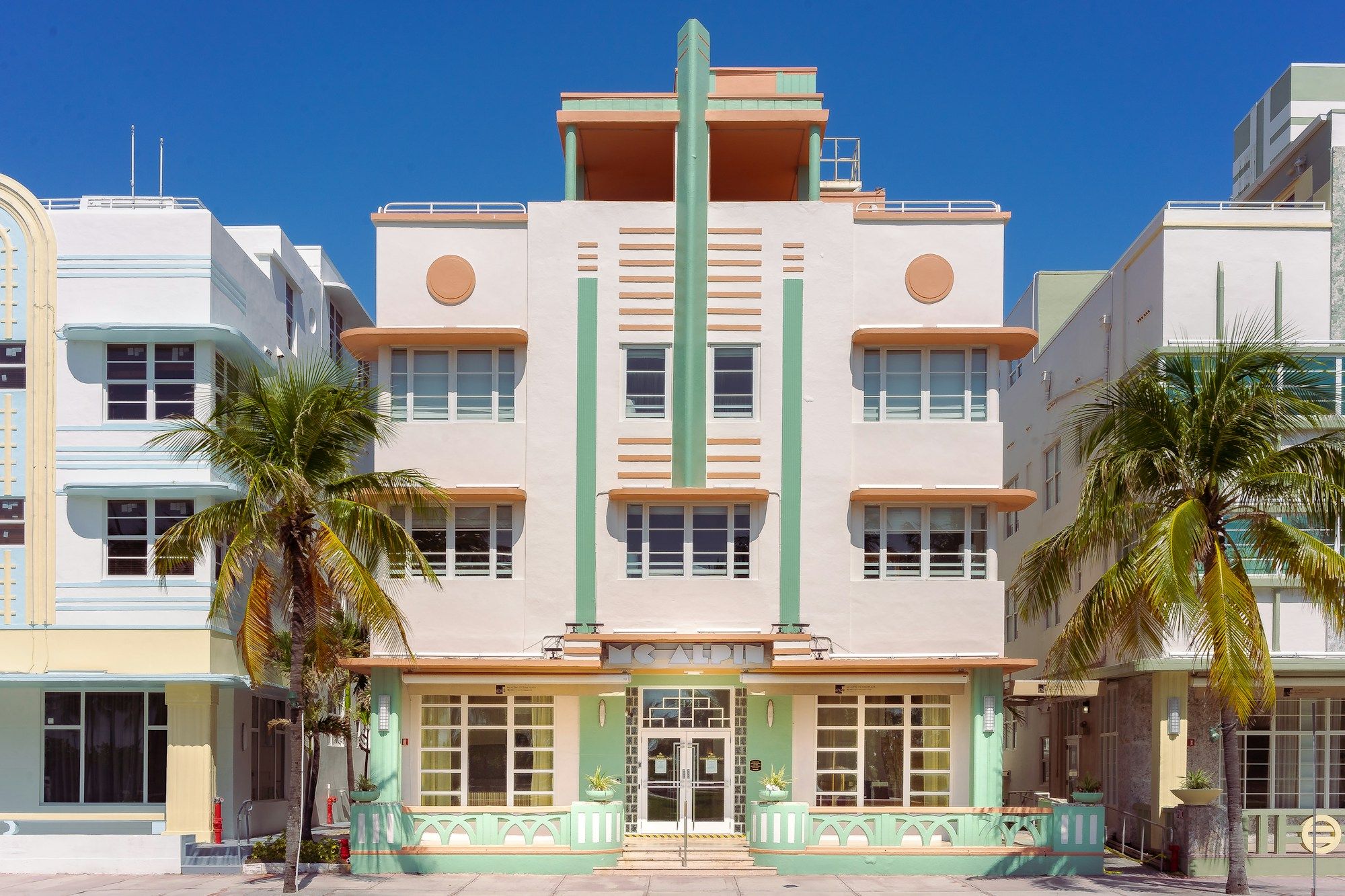 A pastel Art Deco building with palm trees in front, under a deep blue sky in South Beach, Miami Beach.