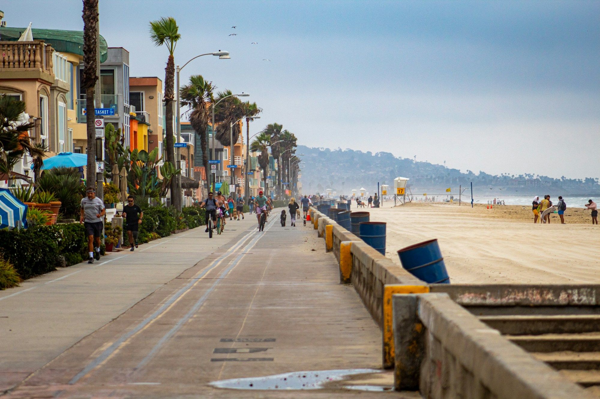 People walking and cycling along the boardwalk at Mission Beach in San Diego, with the beach on the right.