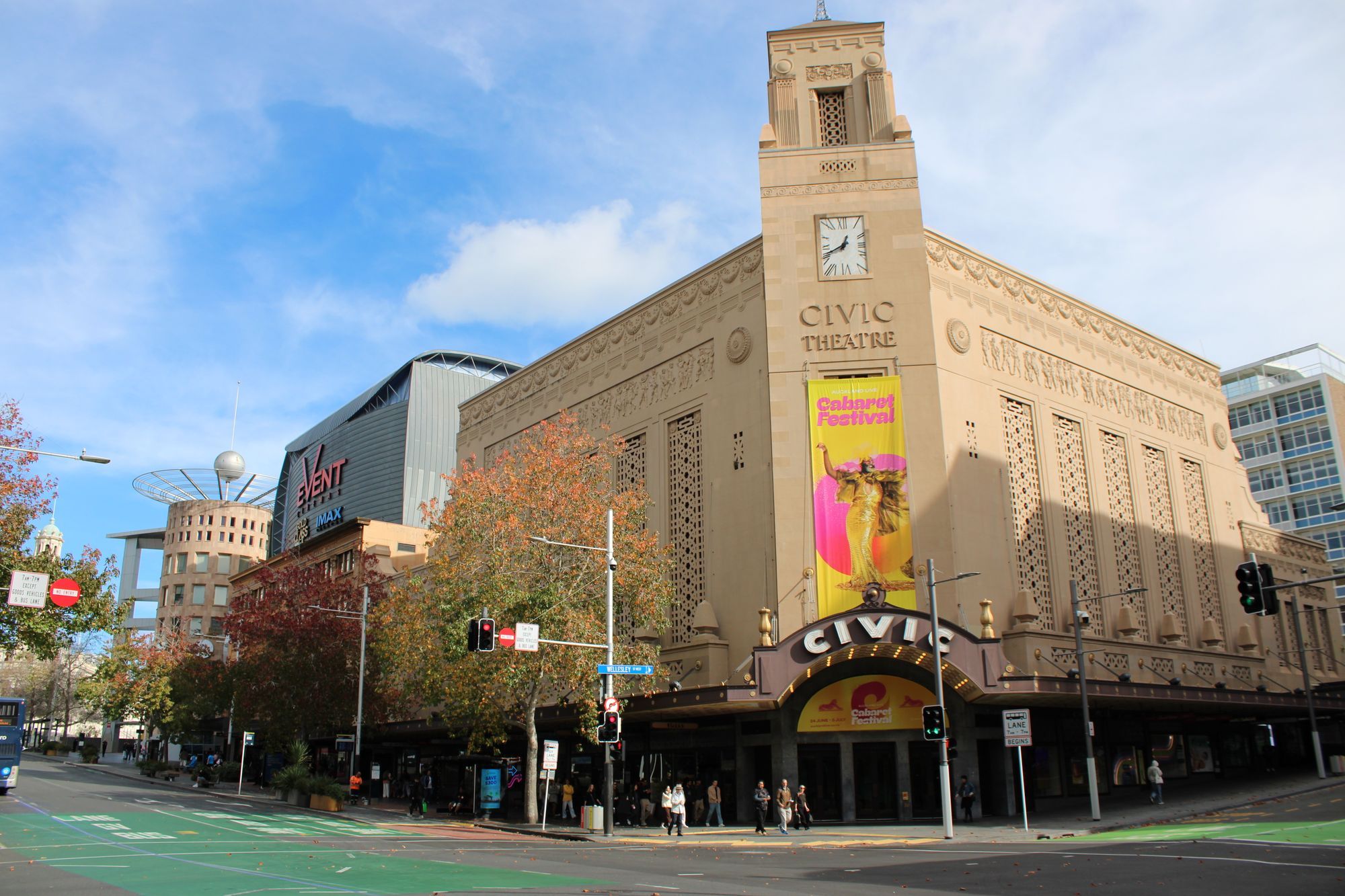 The Civic Theatre on a sunny street corner in central Auckland, with autumn trees and people crossing the street.