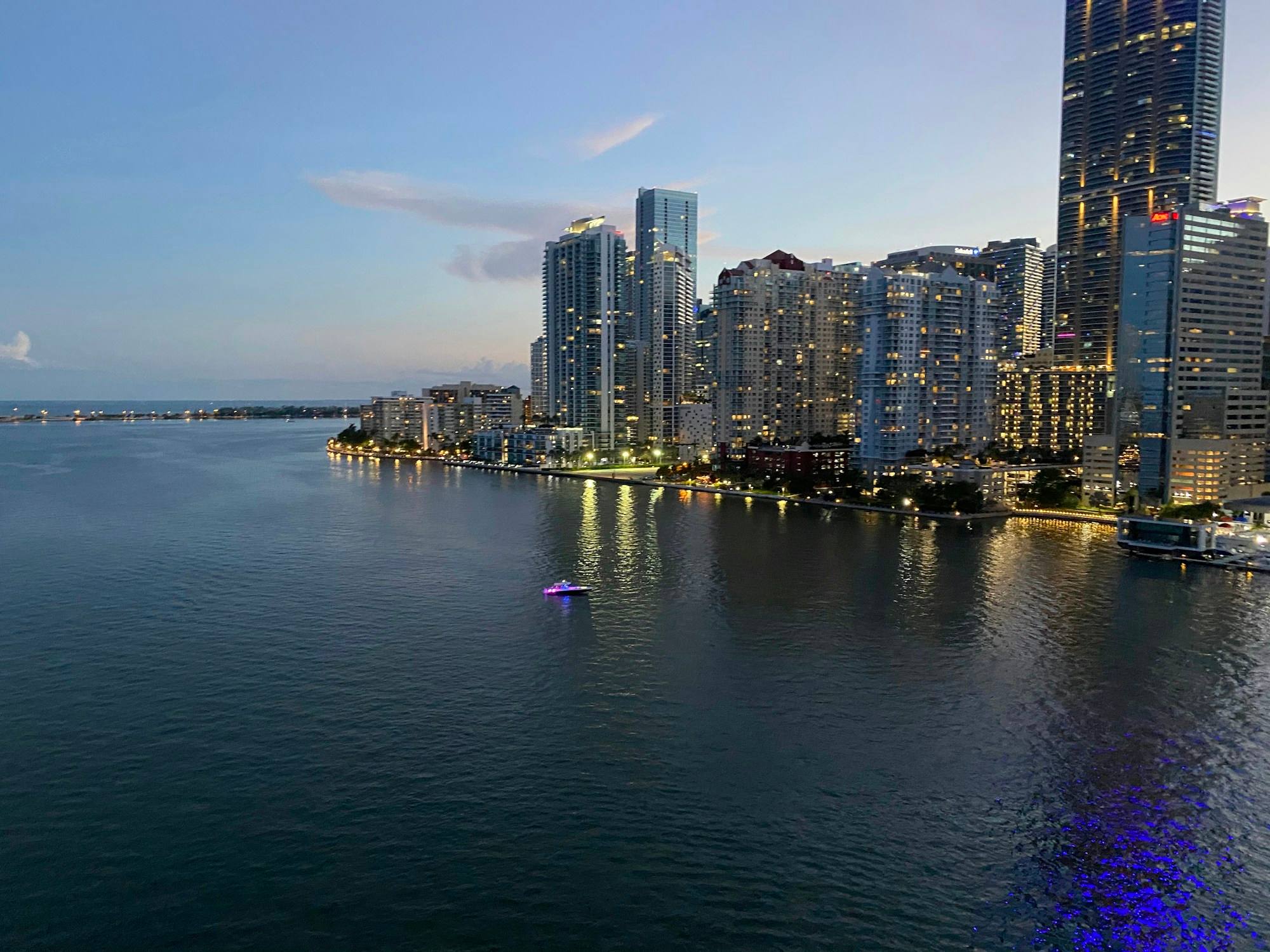 The Brickell skyline in Miami at dusk, with lit towers along the shore and dark water in front.