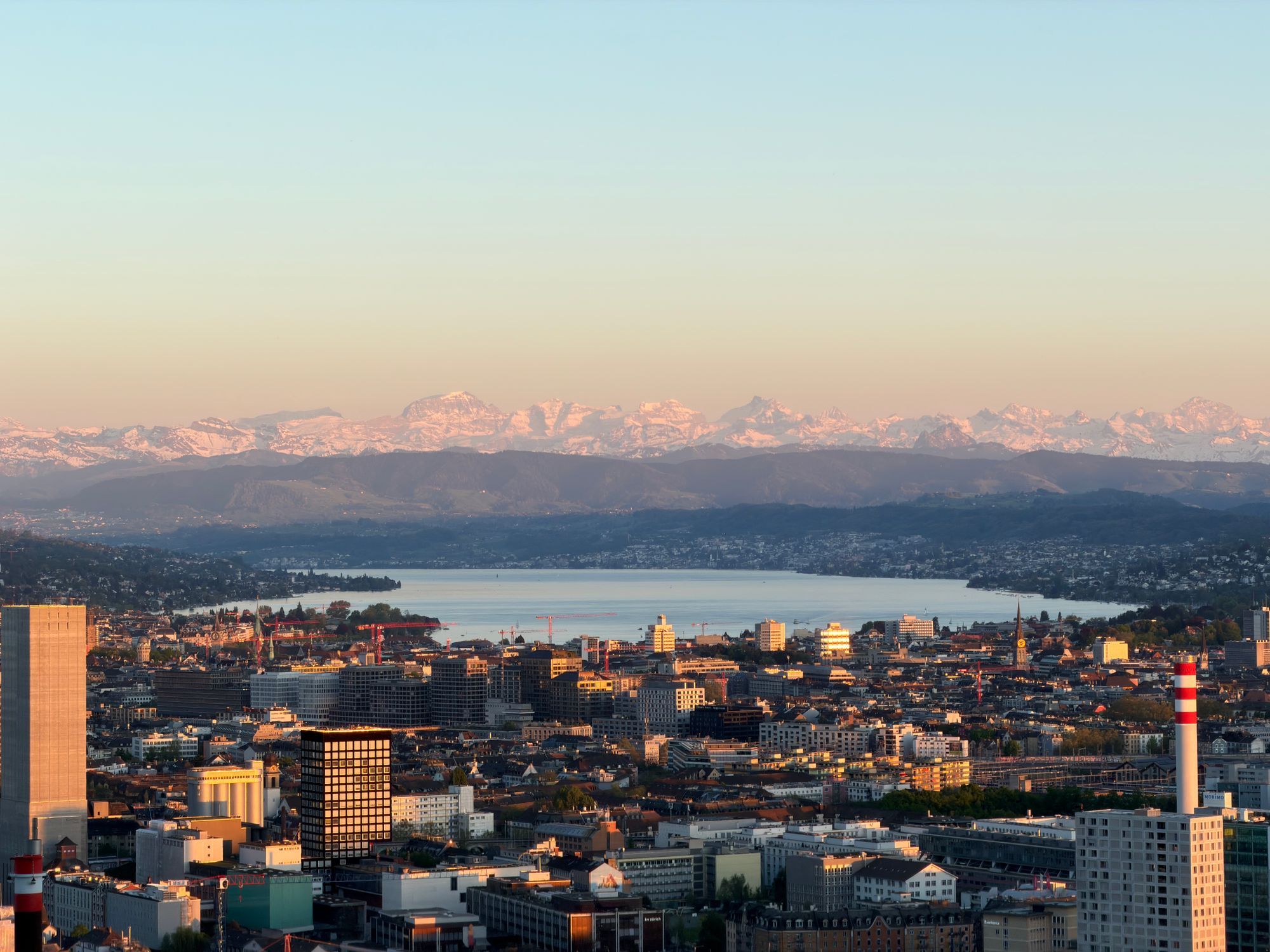 Zurich at sunset with Lake Zurich and the snow-covered Alps in the distance.