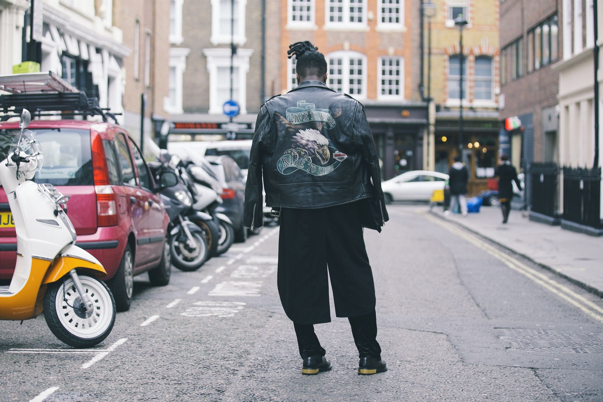 Someone walking down Brewer Street in Soho, London, past parked scooters and cars