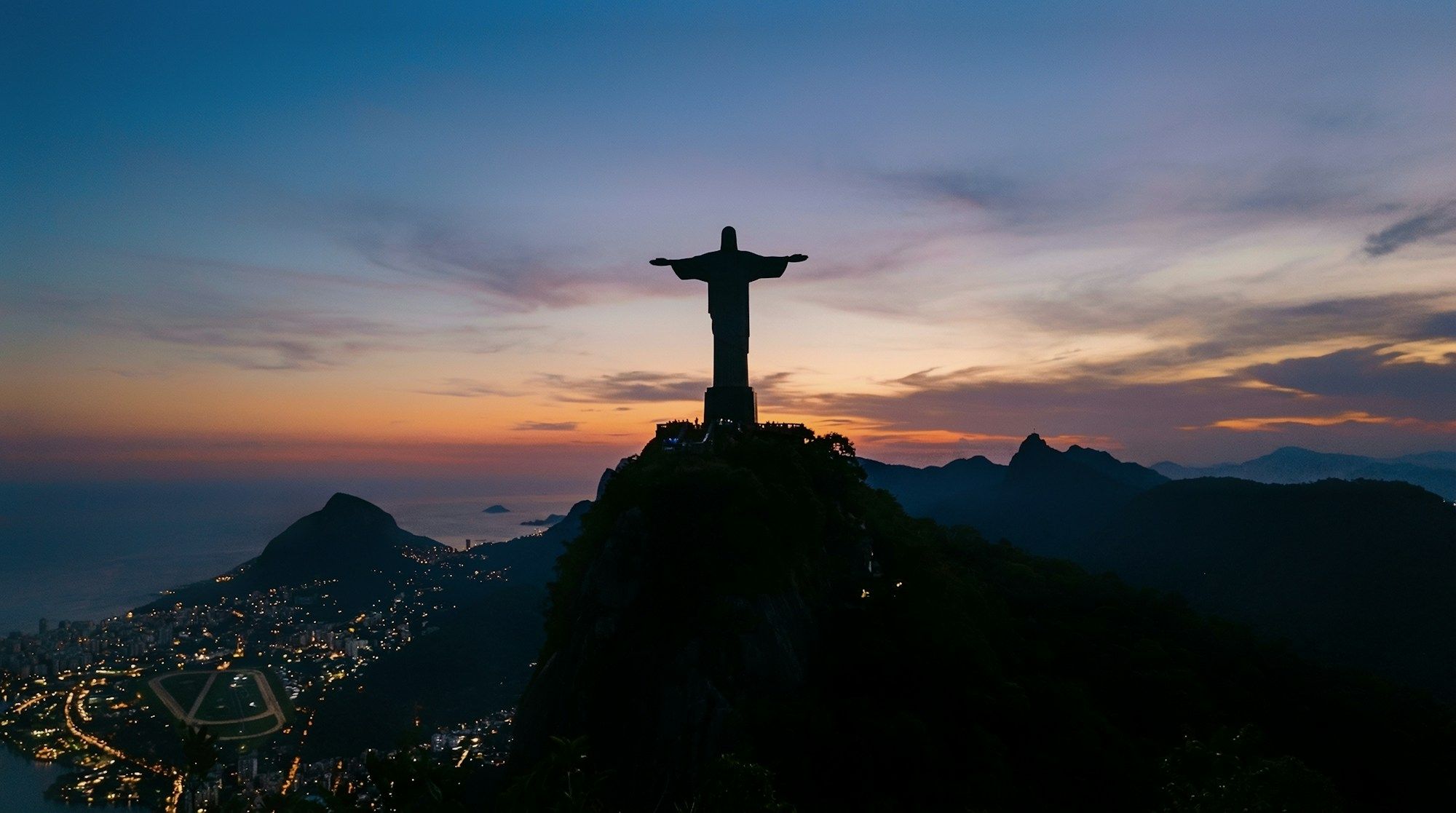 The Christ the Redeemer statue on Corcovado at dusk, above the lights of Rio de Janeiro.