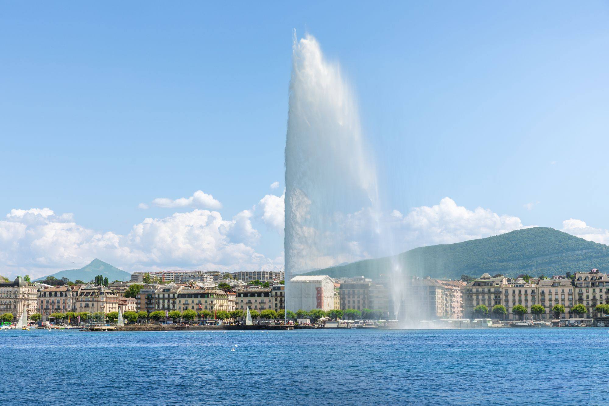 The Jet d'Eau rising above the Lake Geneva waterfront in Geneva, with the hills behind.