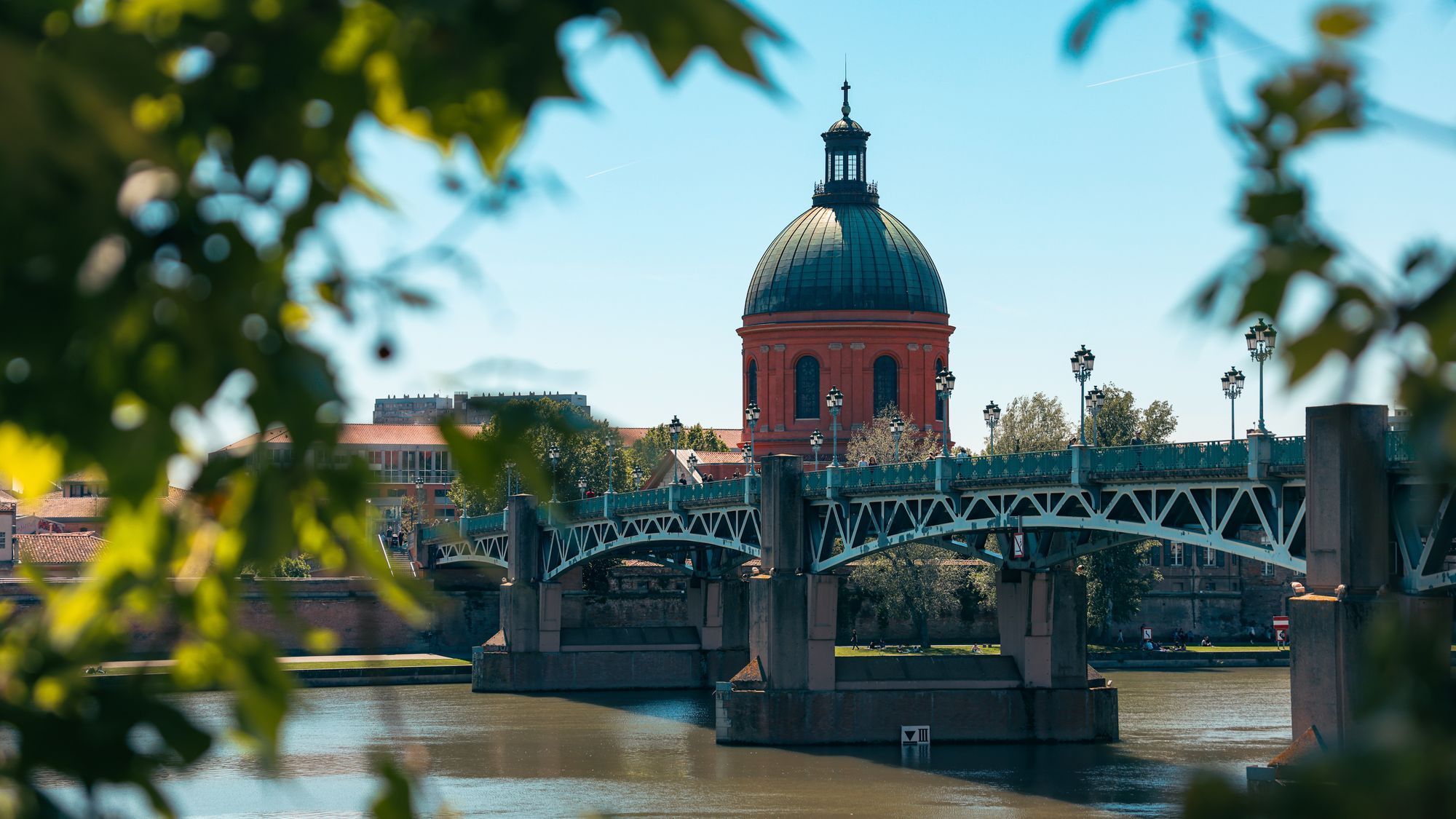The Pont Saint-Pierre and the red dome of La Grave over the Garonne in Toulouse, seen through leaves.