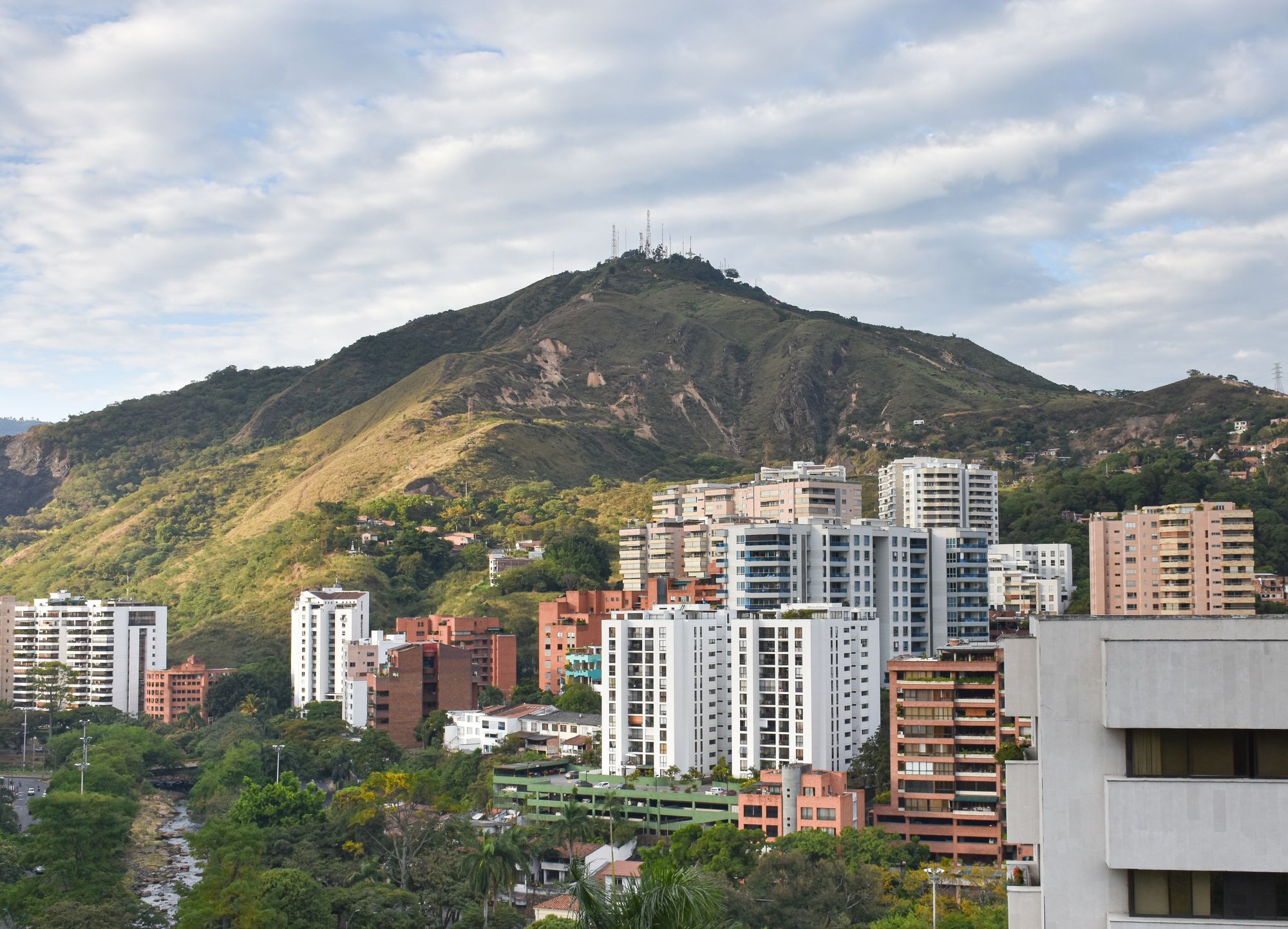 Apartment towers of Cali below a green hill topped with radio masts.