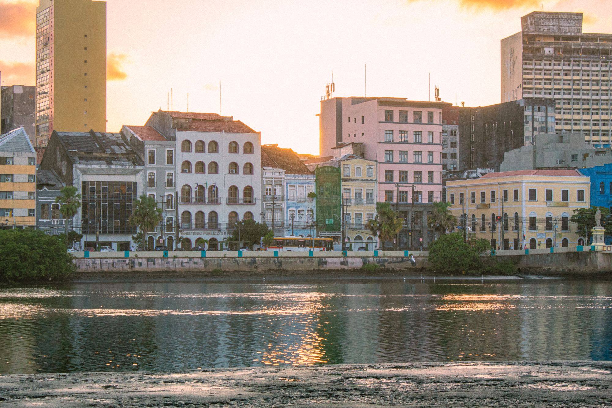 Historic buildings along the river in Recife at sunset, with their reflections on the water.