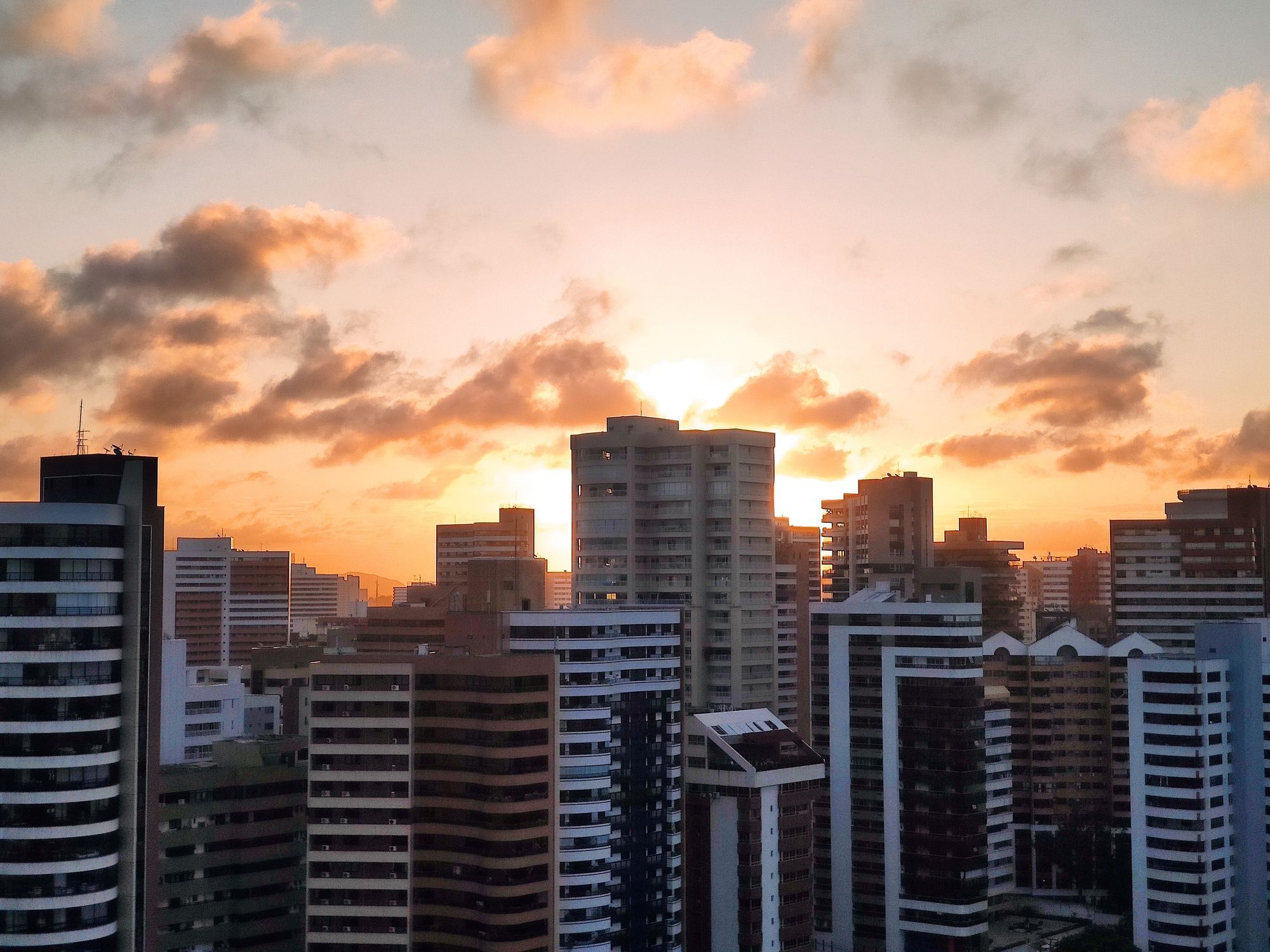 Apartment towers in the Aldeota district of Fortaleza against a sunset sky with orange clouds.
