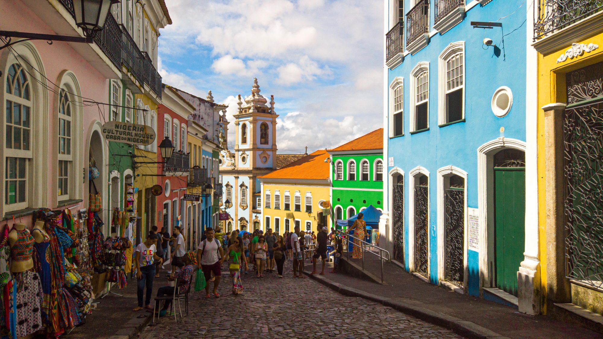 People walking along a cobbled street lined with colorful colonial houses in the Pelourinho district of Salvador.