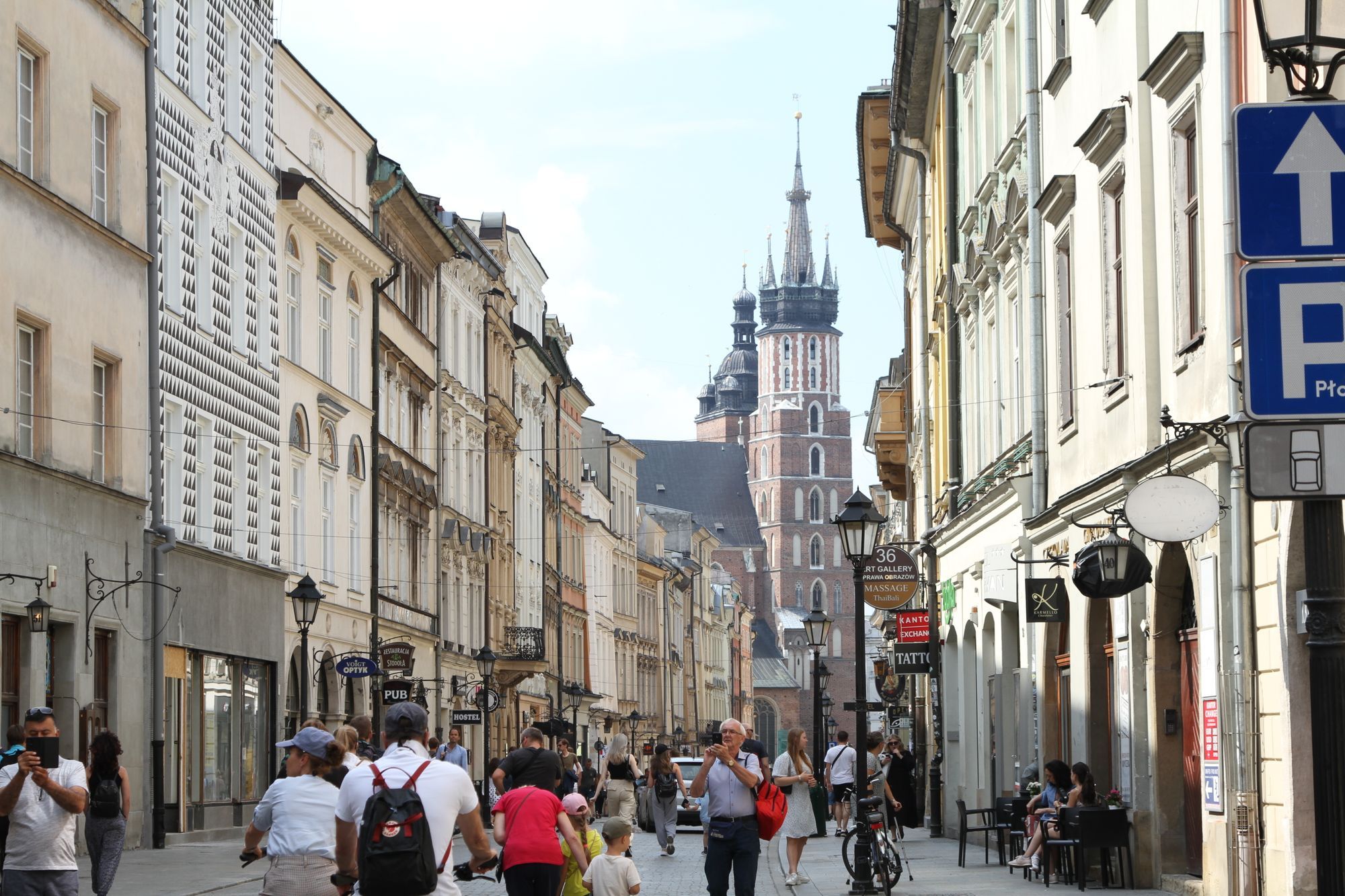 People walking along a street of tall townhouses in Kraków, with the tower of St Mary's Basilica in the distance.