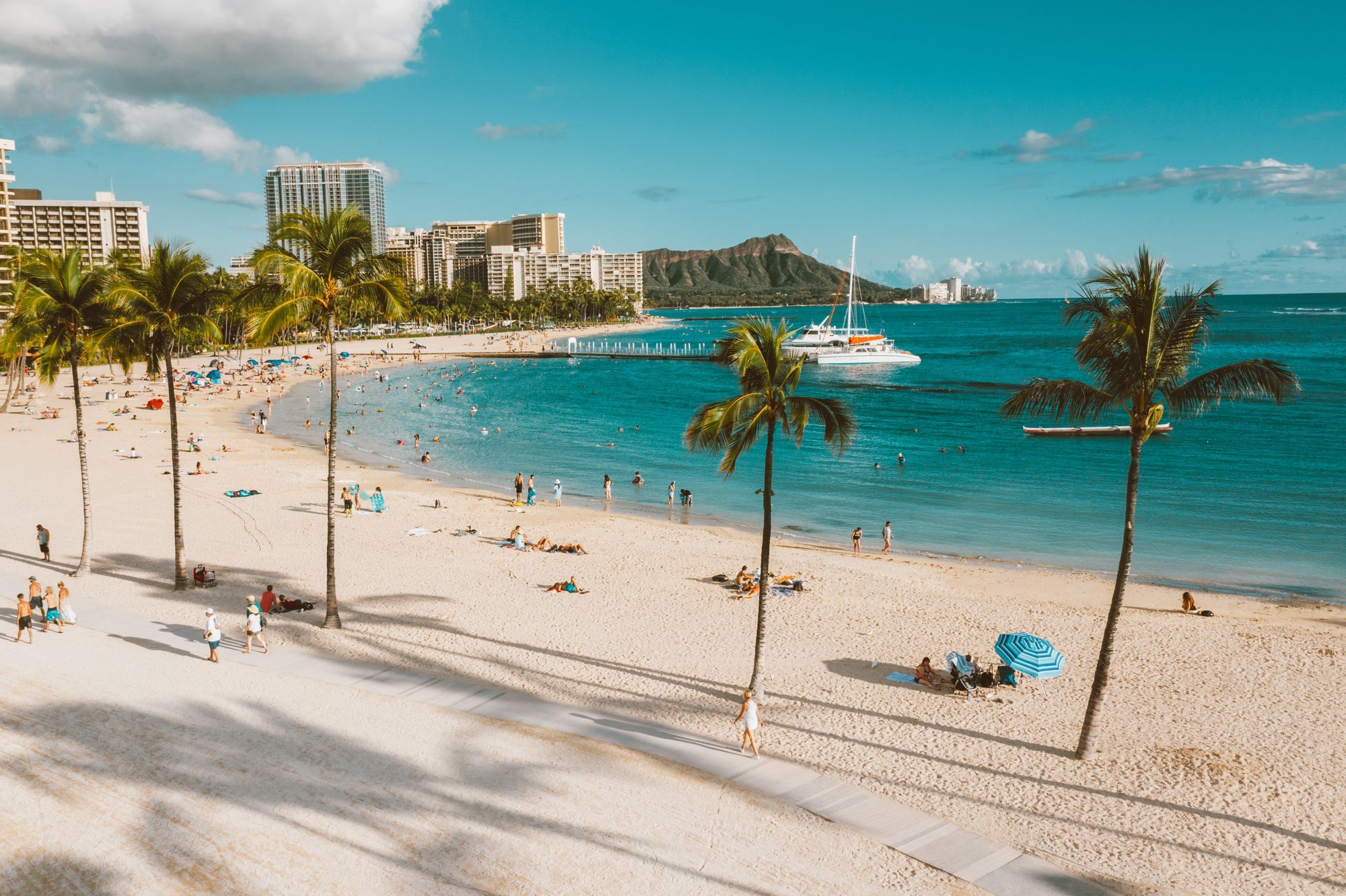 Waikiki Beach with palm trees and sunbathers, and Diamond Head in the distance.