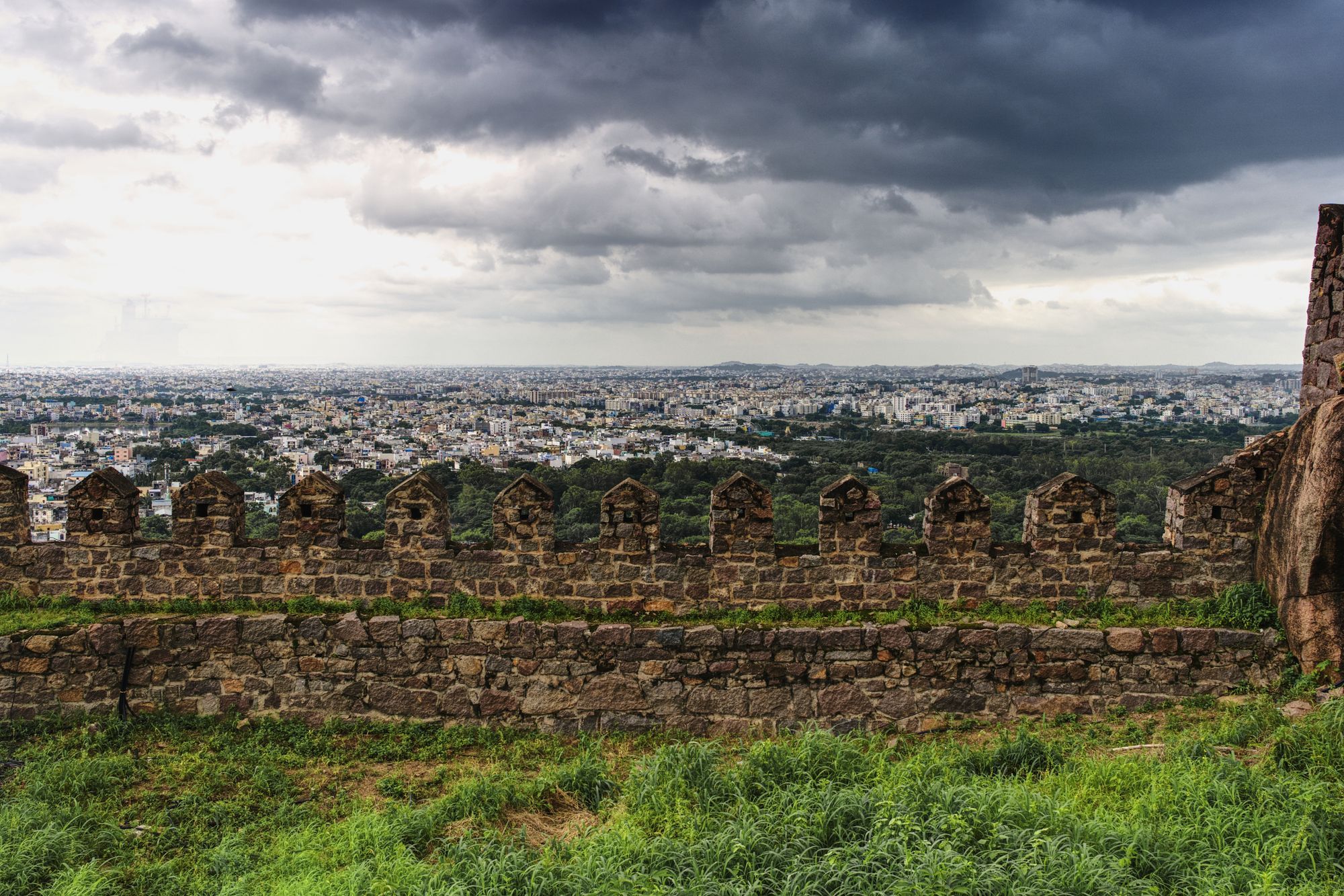 A view over the city of Hyderabad from the stone ramparts of Golconda Fort, under dark clouds.