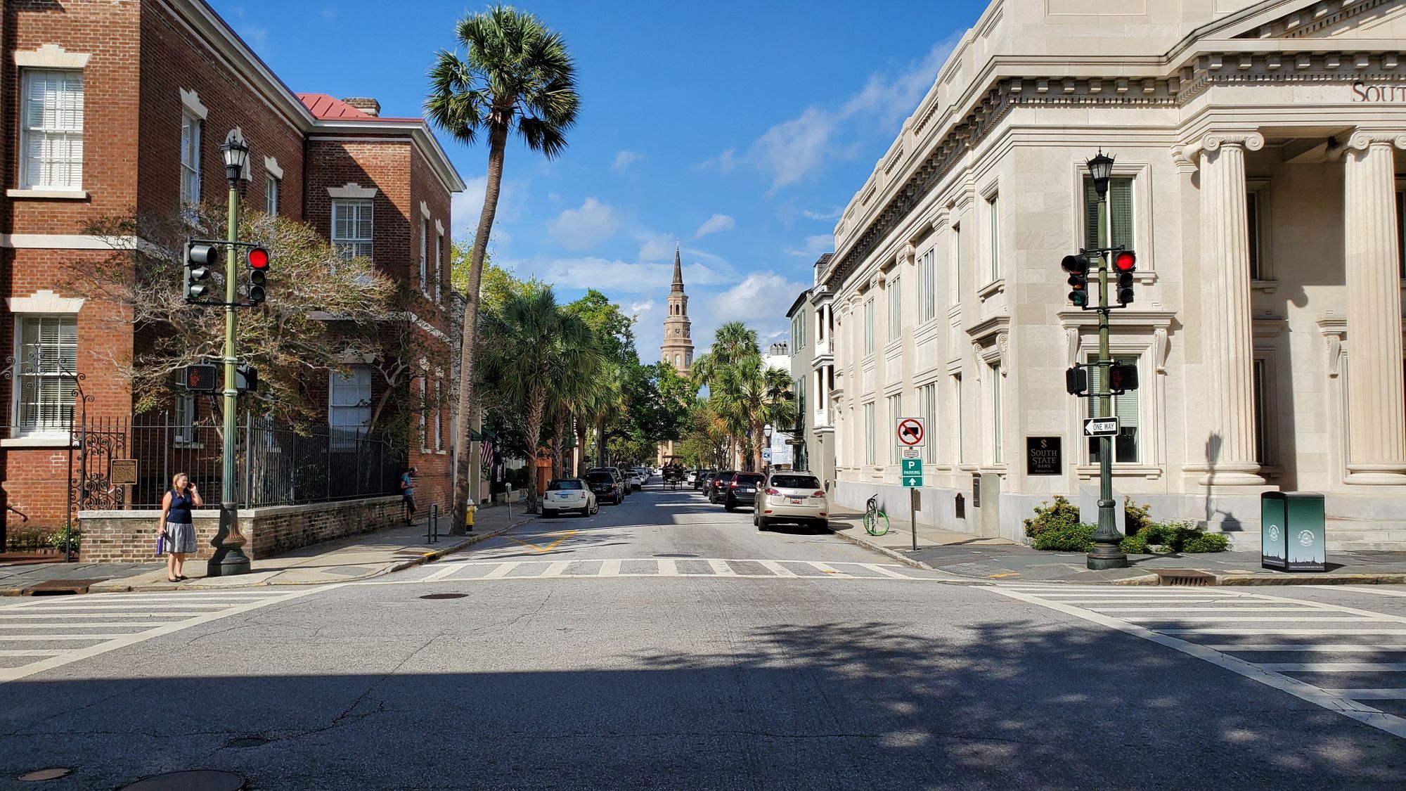 A sunny Charleston street with historic buildings, a palm tree and a church spire in the distance.