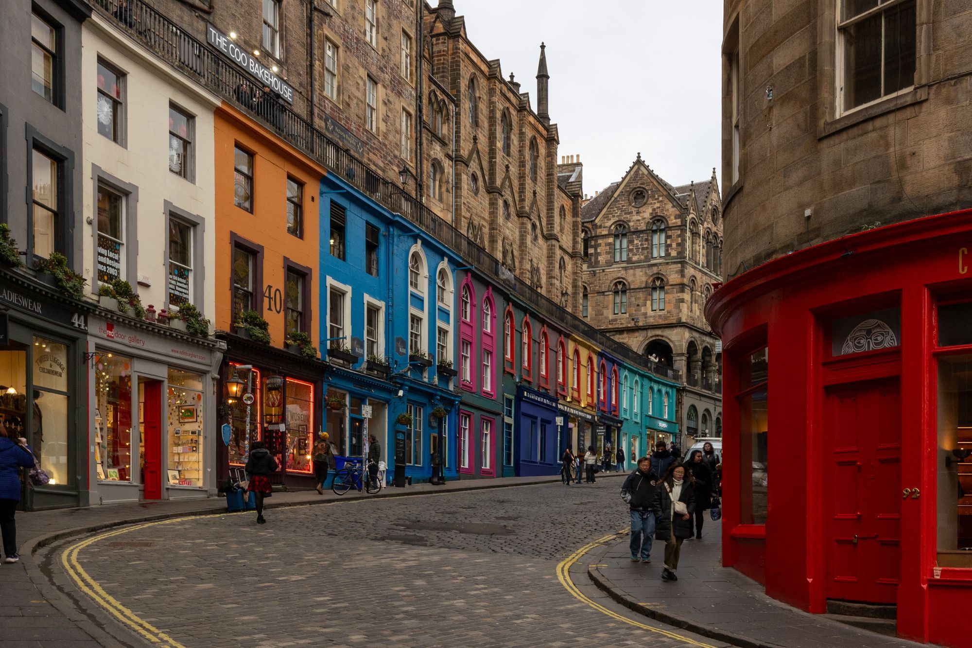 Colorful shopfronts curving along Victoria Street in Edinburgh's Old Town, with a few people walking.