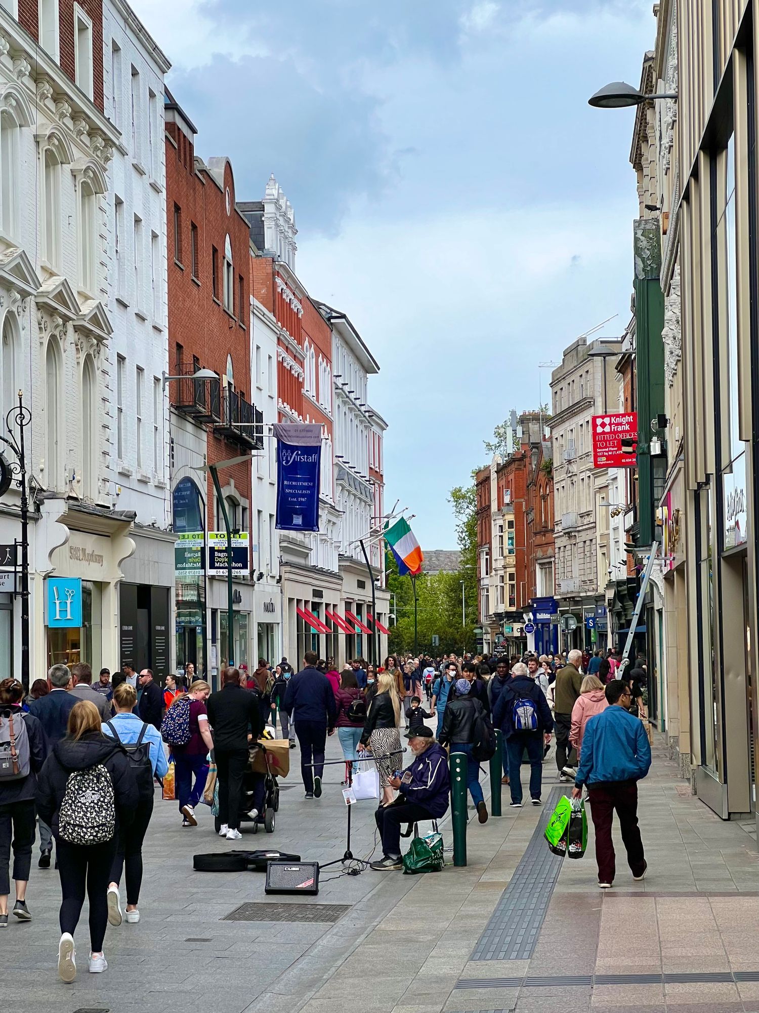 Shoppers walking down Grafton Street in Dublin, with shopfronts on both sides.