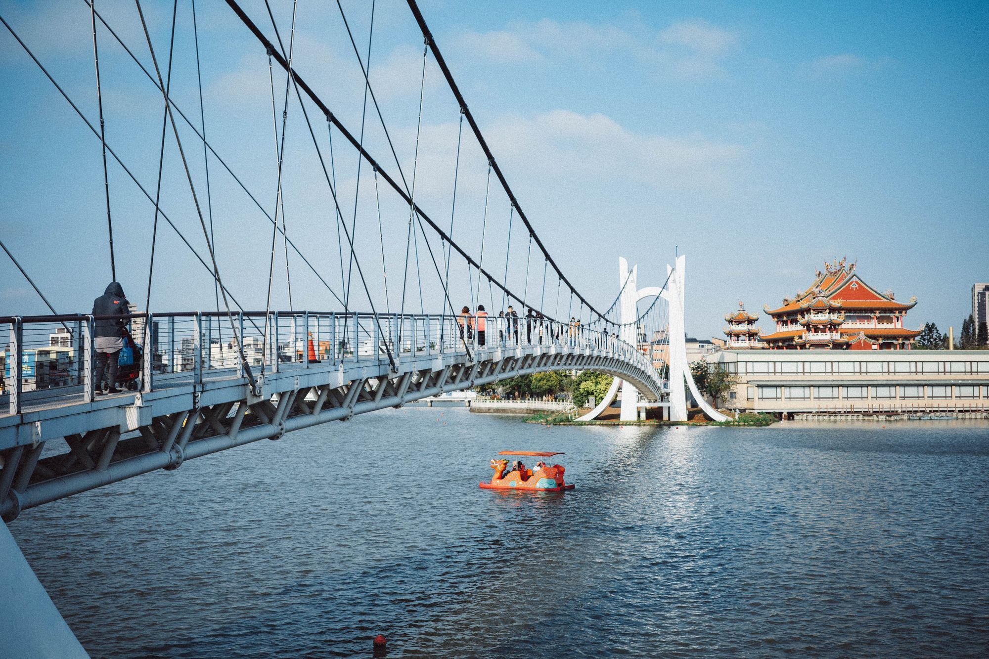 A suspension footbridge across a lake with a temple on the far shore in Taoyuan City.