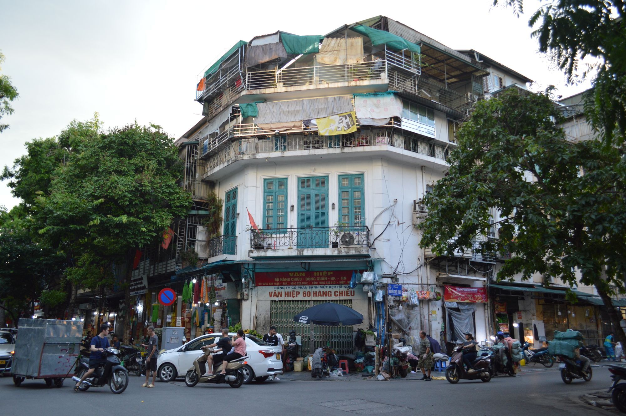 A street corner in the Old Quarter of Hanoi, with an old shophouse above and motorbikes and a car passing below.
