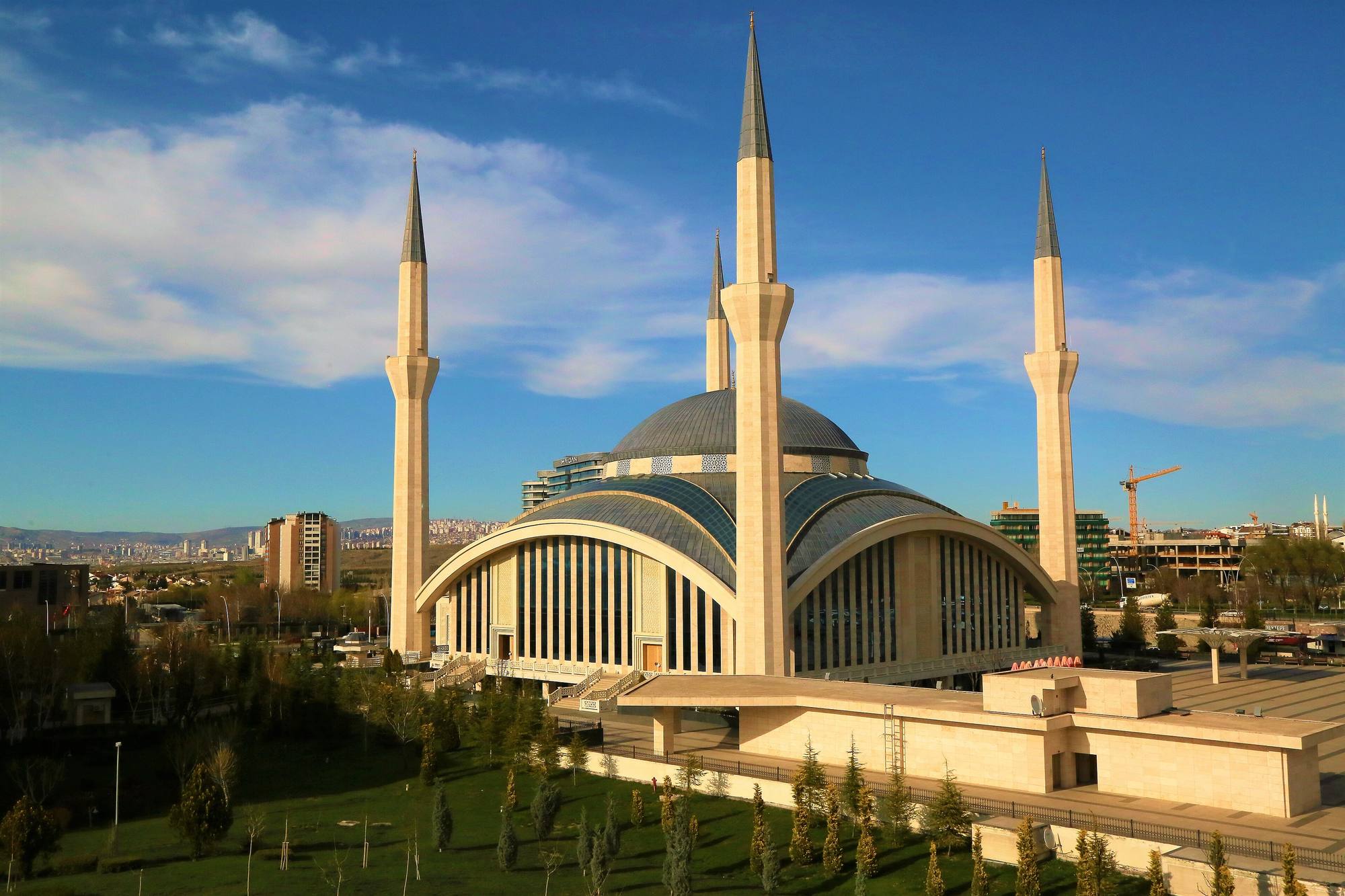 The four minarets and curved roofs of the Ahmet Hamdi Akseki Mosque in Ankara under a blue sky with clouds.