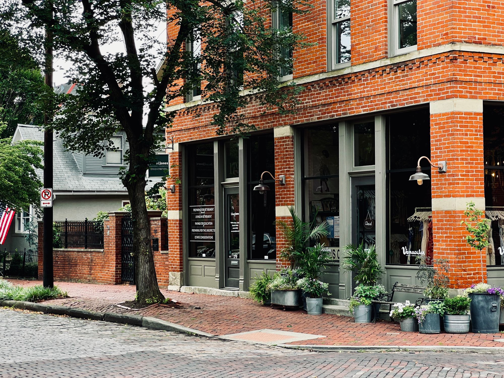 A brick corner building with plants outside its doors on a cobblestone street in German Village, Columbus.