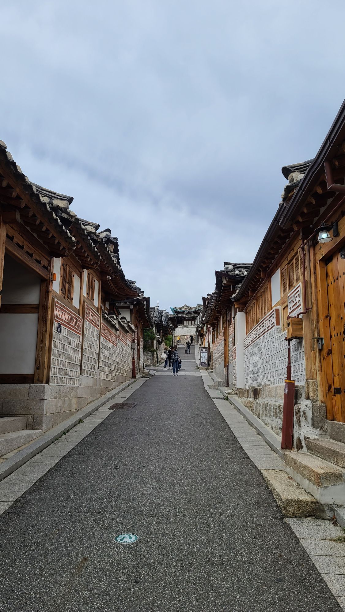 A narrow alley of traditional hanok houses in Bukchon Hanok Village in Seoul, with a person walking far ahead.