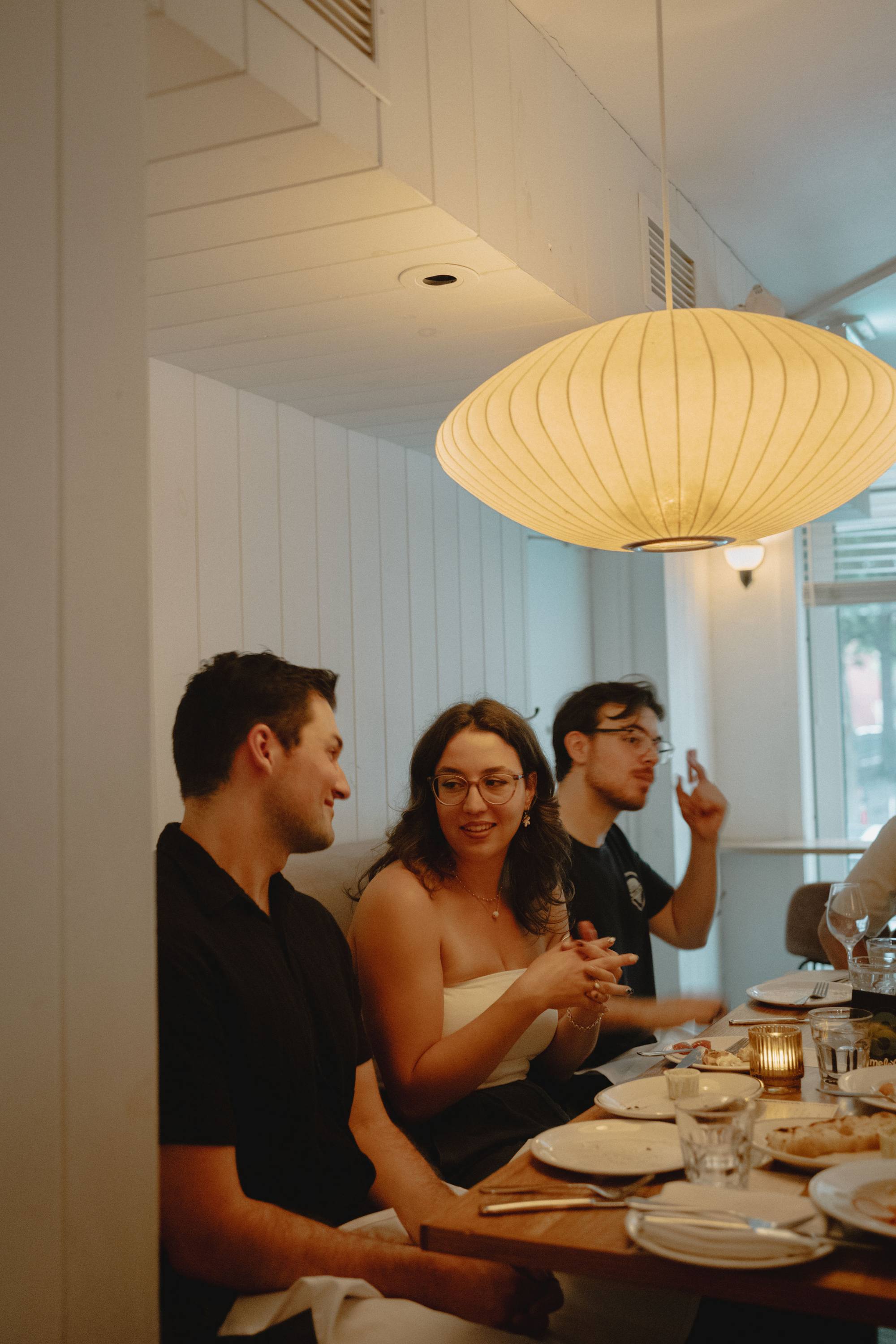 Three people laughing at a restaurant table under a paper lantern