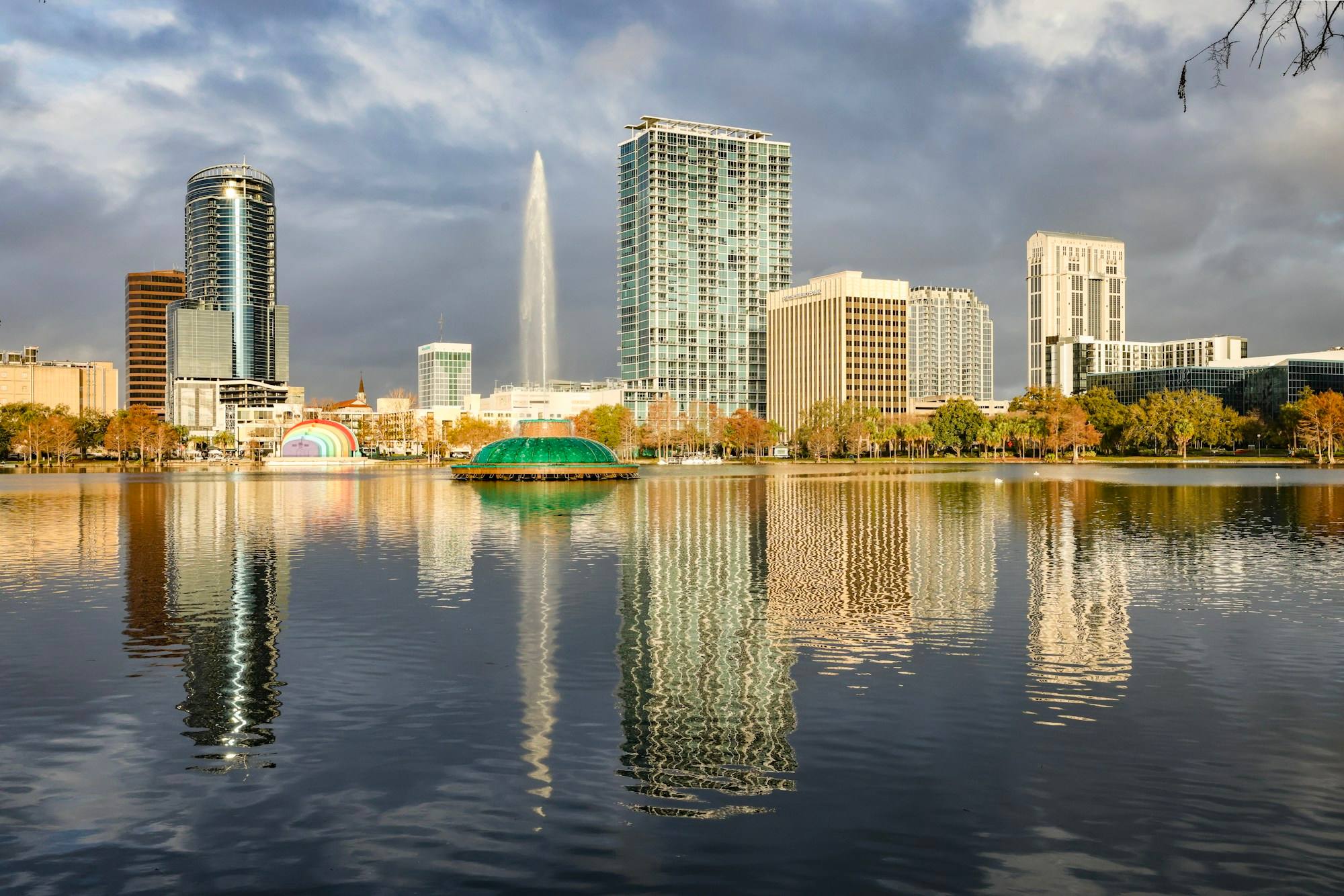 The Orlando skyline across Lake Eola at sunrise, with the park fountain in the middle and the towers reflected in the water.