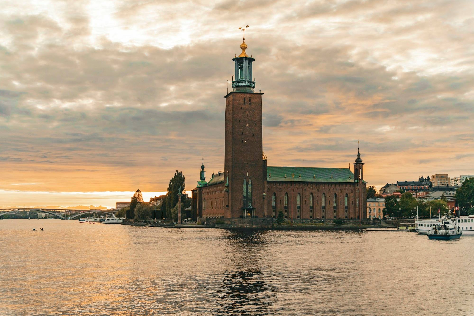 Stockholm City Hall and its tower on the waterfront at sunset, with golden light on the water in front.