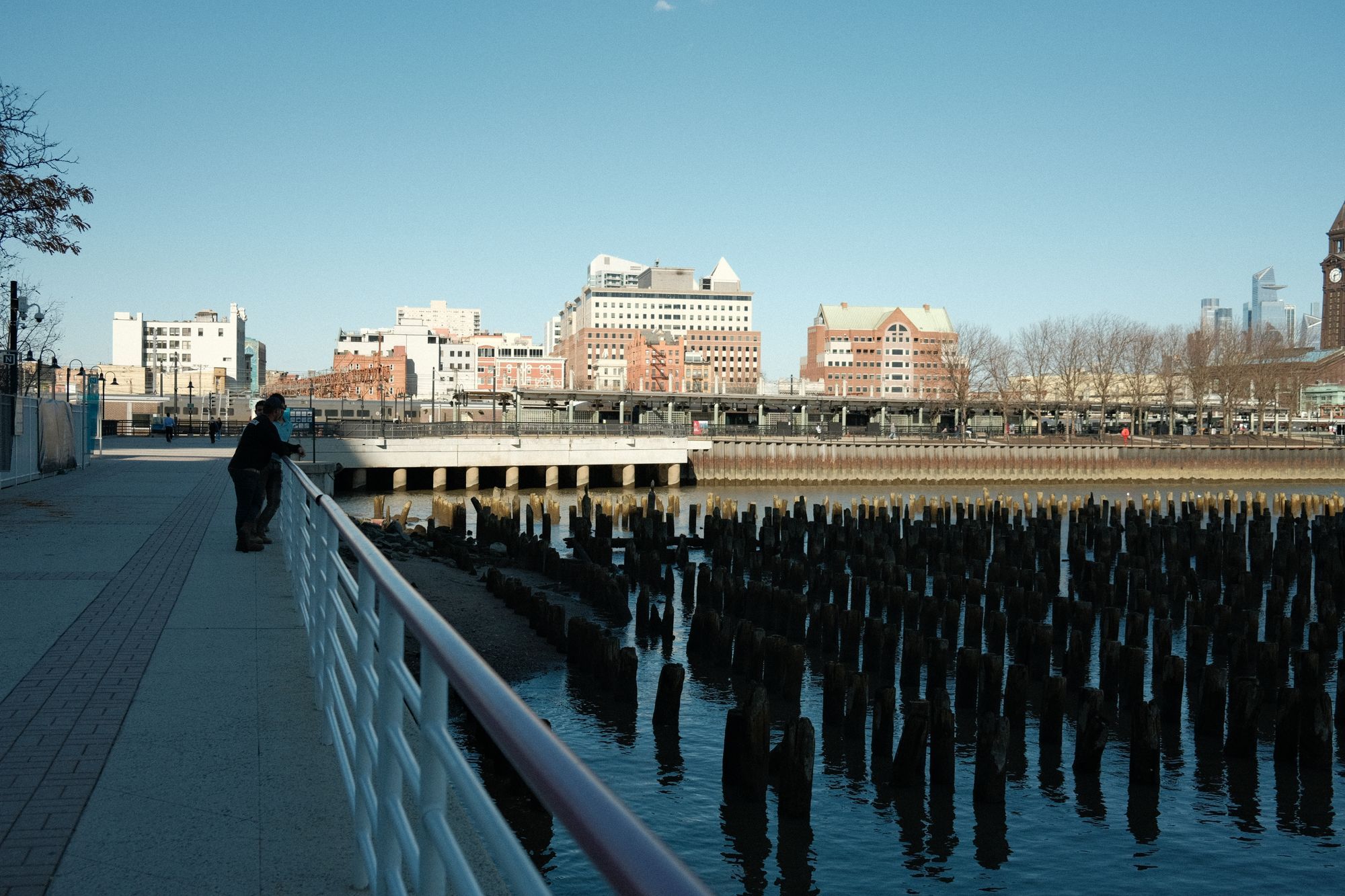 The Hudson waterfront walkway in Jersey City with old pier pilings in the water.