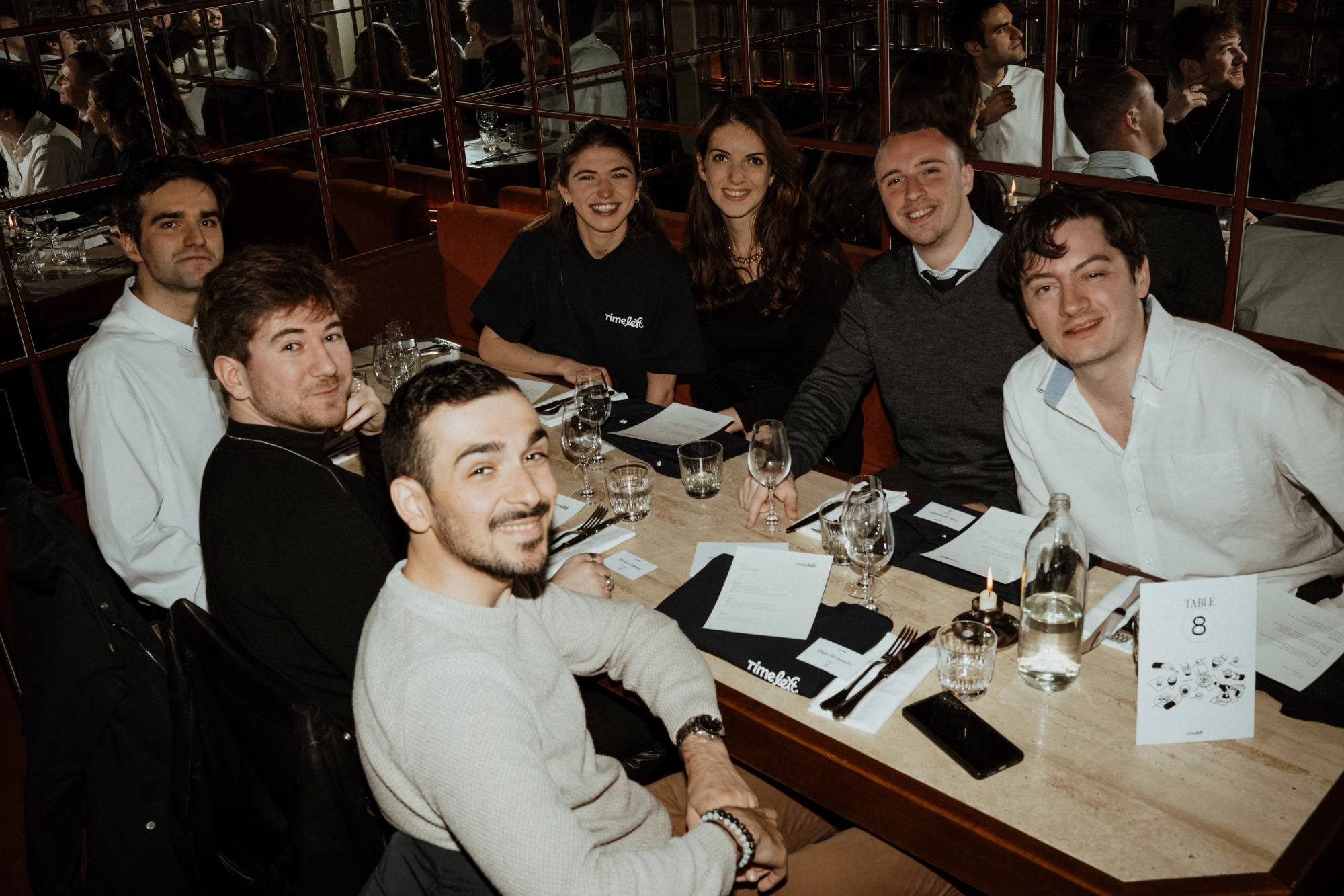 Seven guests smiling at the camera around a long dinner table