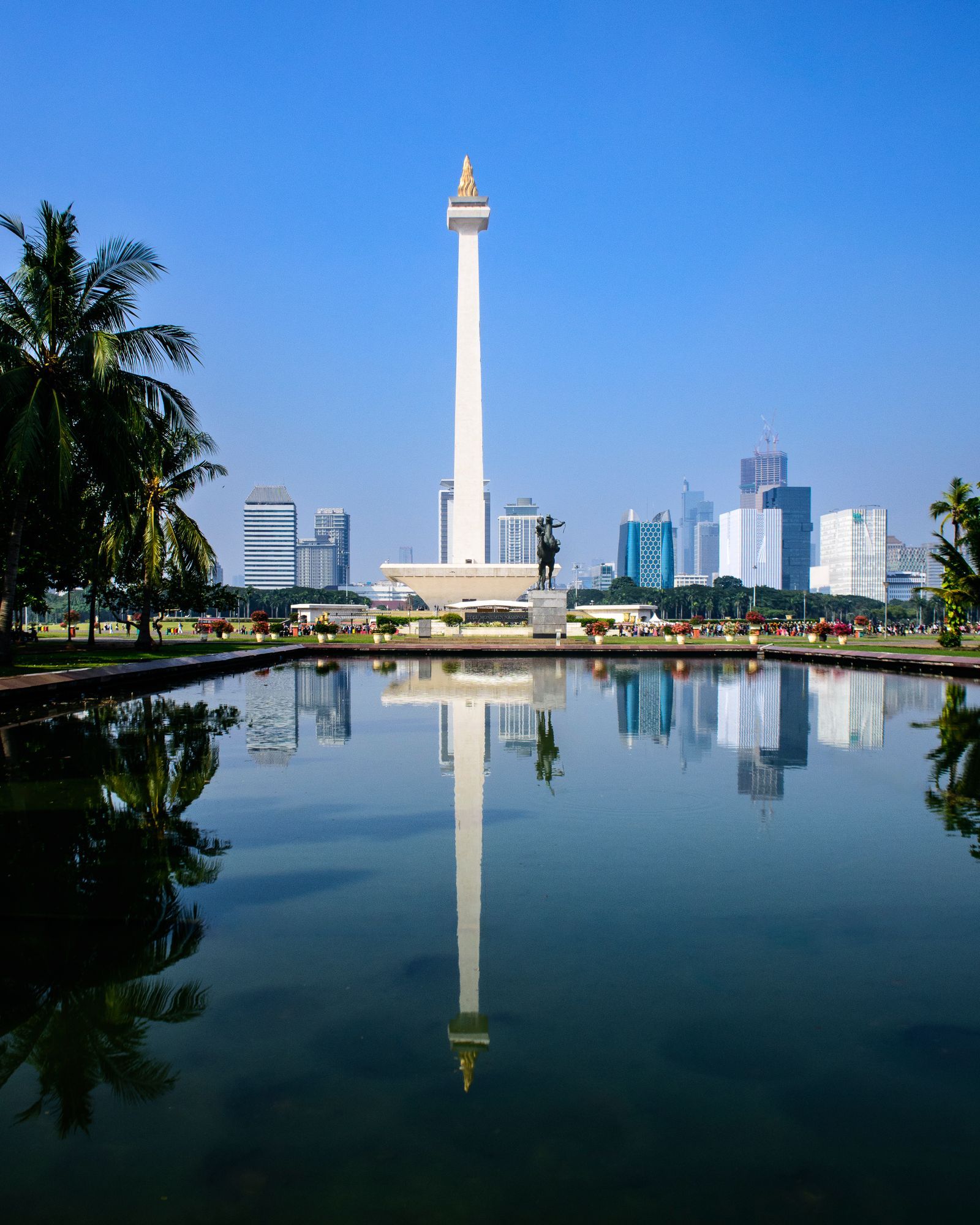 The Monas National Monument in Jakarta, with its reflection in a pond and the city skyline behind.