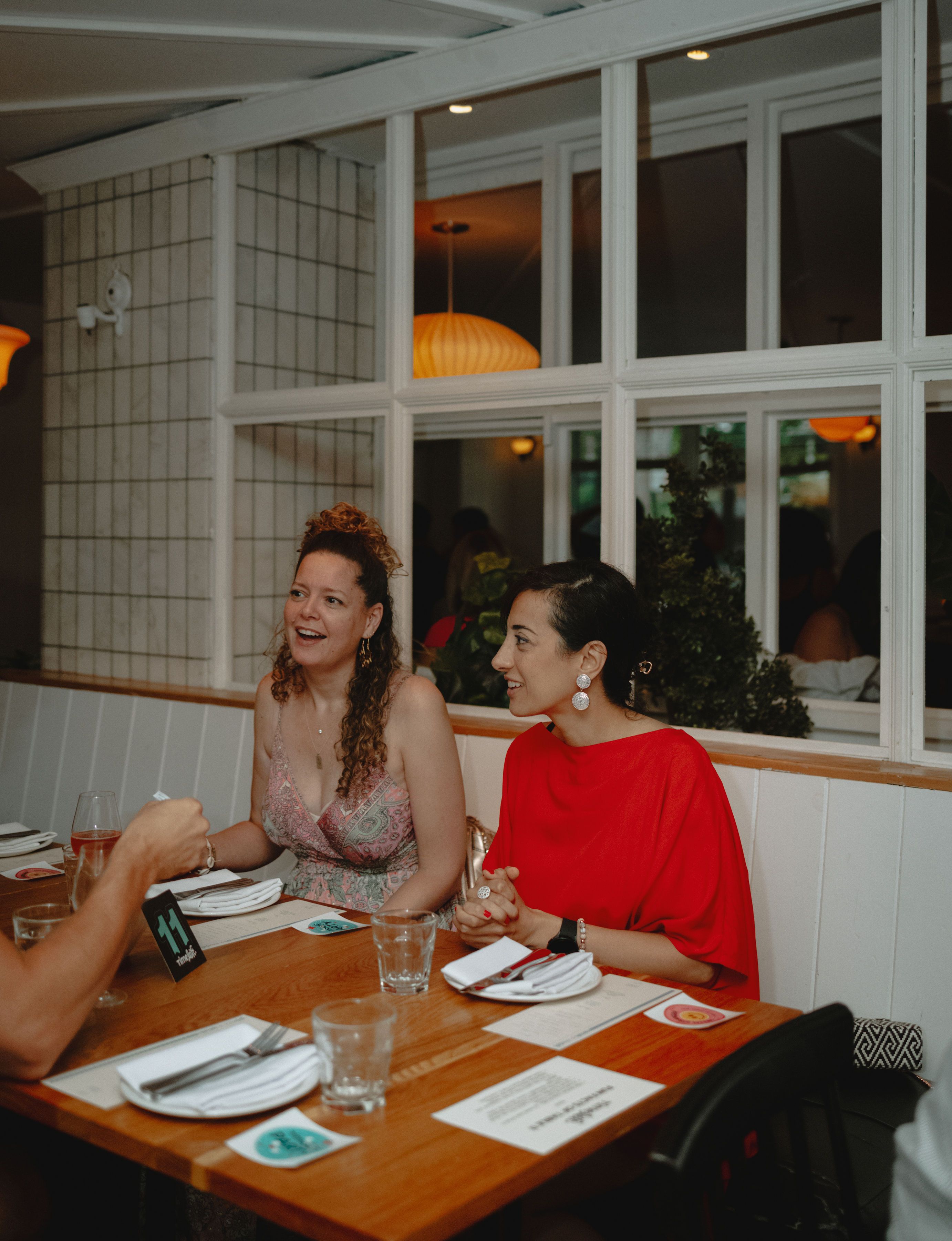 Two women laughing together at a Timeleft dinner table by a big window
