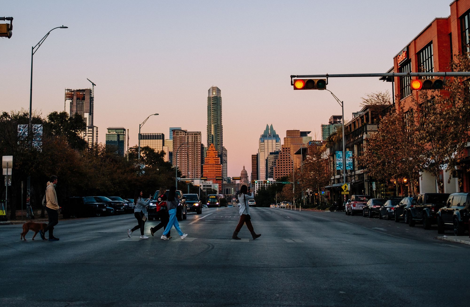 People walking across South Congress Avenue in Austin at sunset, with the downtown towers at the end of the street