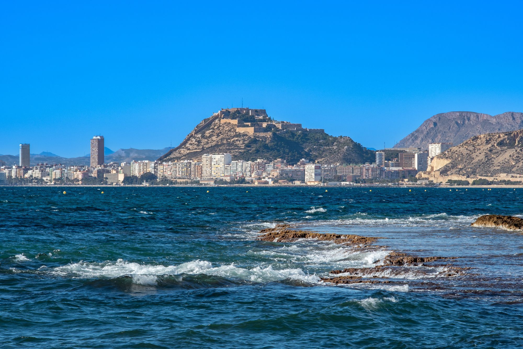 Santa Bárbara Castle above the coastline of Alicante, seen from the rocky shore.
