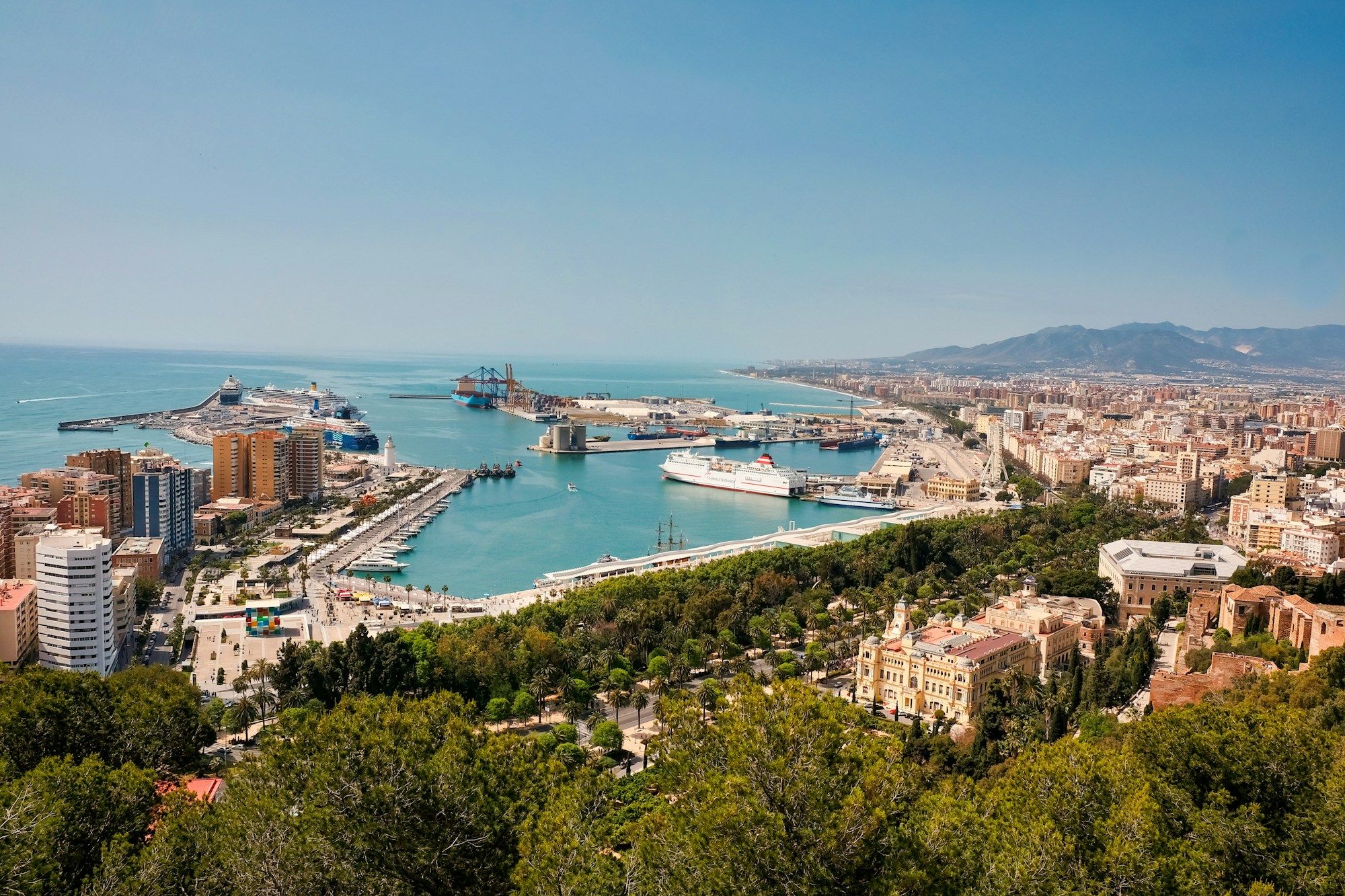Málaga's port and city center seen from Gibralfaro hill, with cruise ships in the harbor and the sea behind.