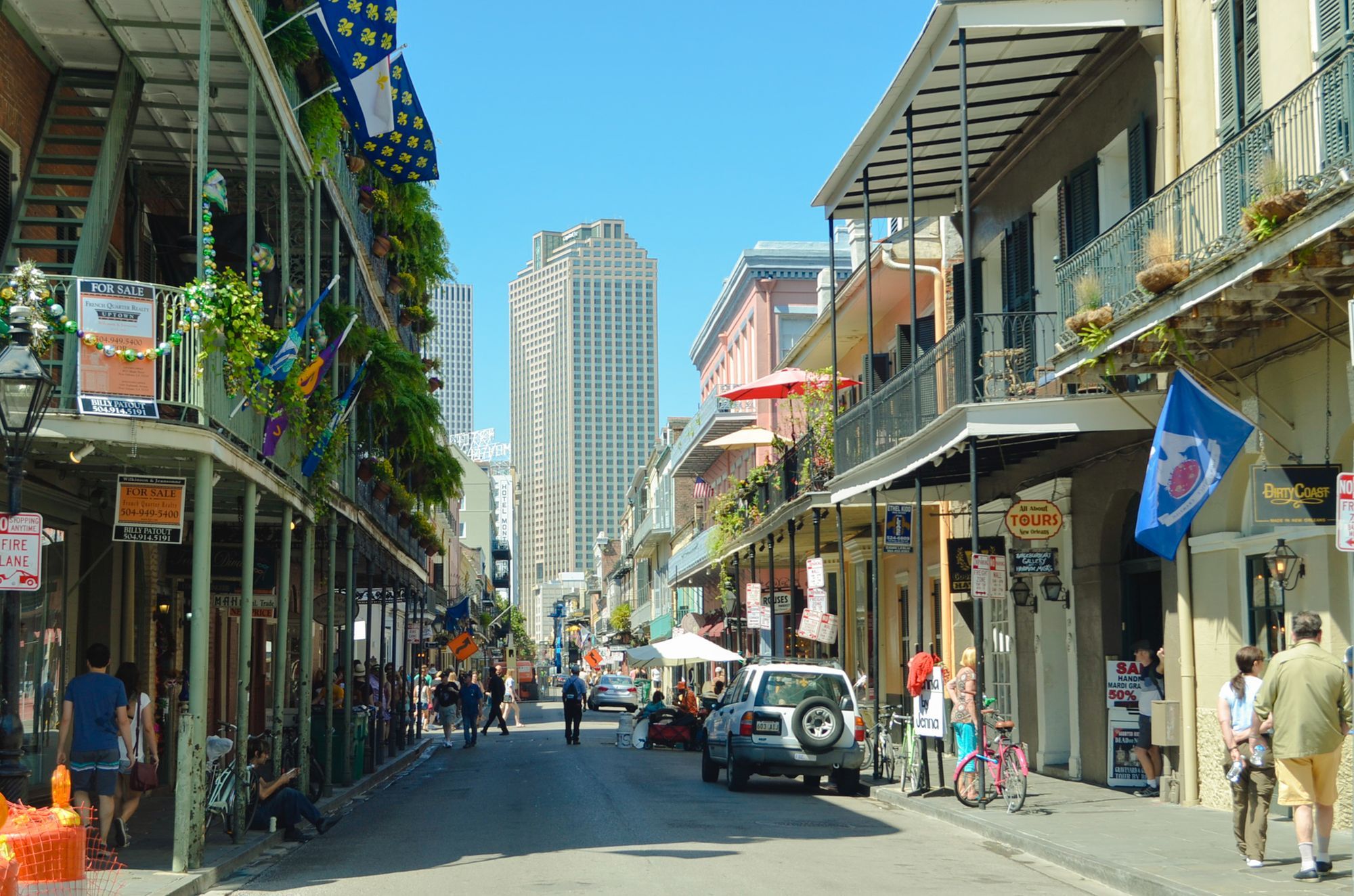 A French Quarter street in New Orleans with iron balconies, pedestrians and a tower block in the distance.