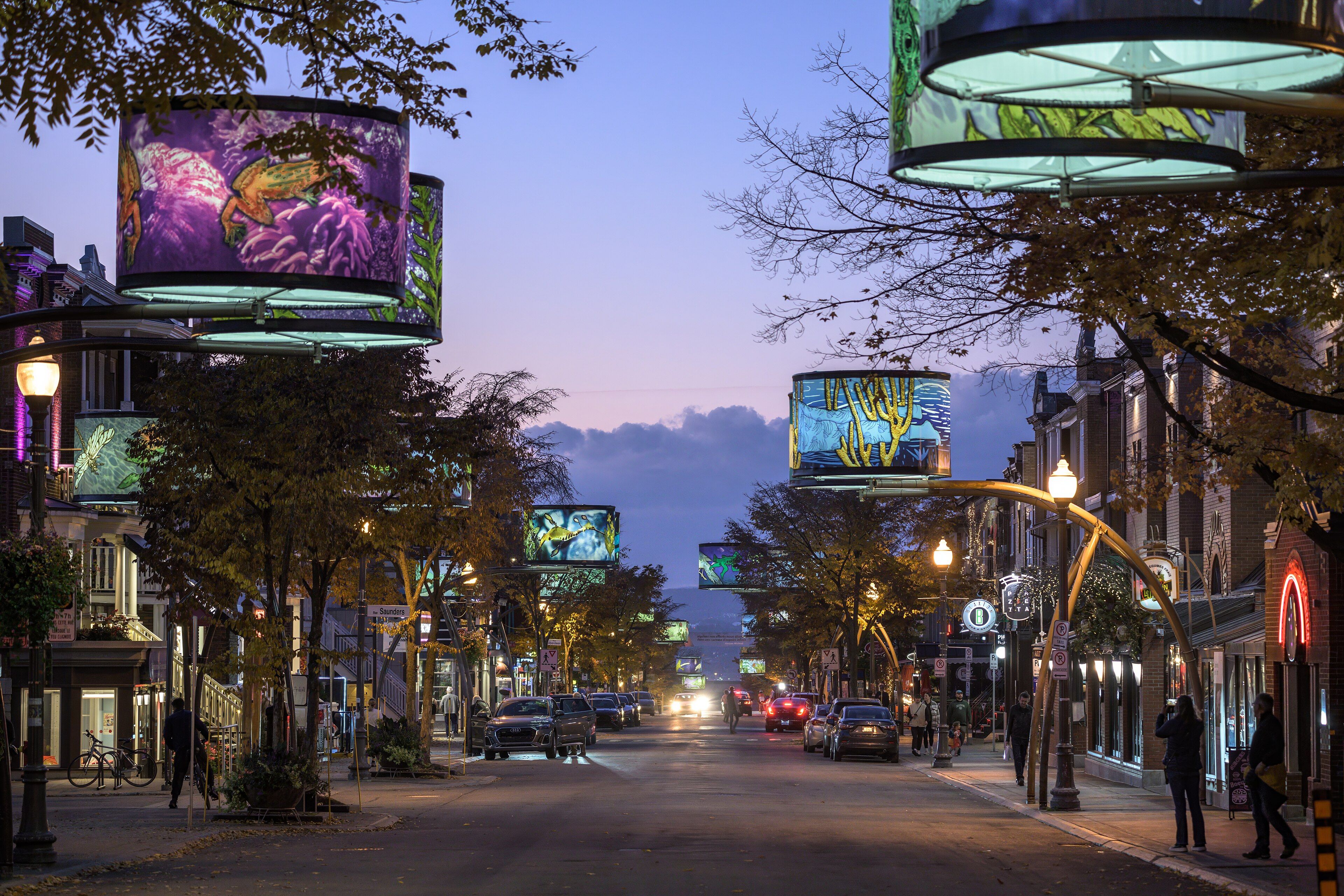 Avenue Cartier in the Montcalm district of Quebec City at dusk, with illuminated panels hung over the street.