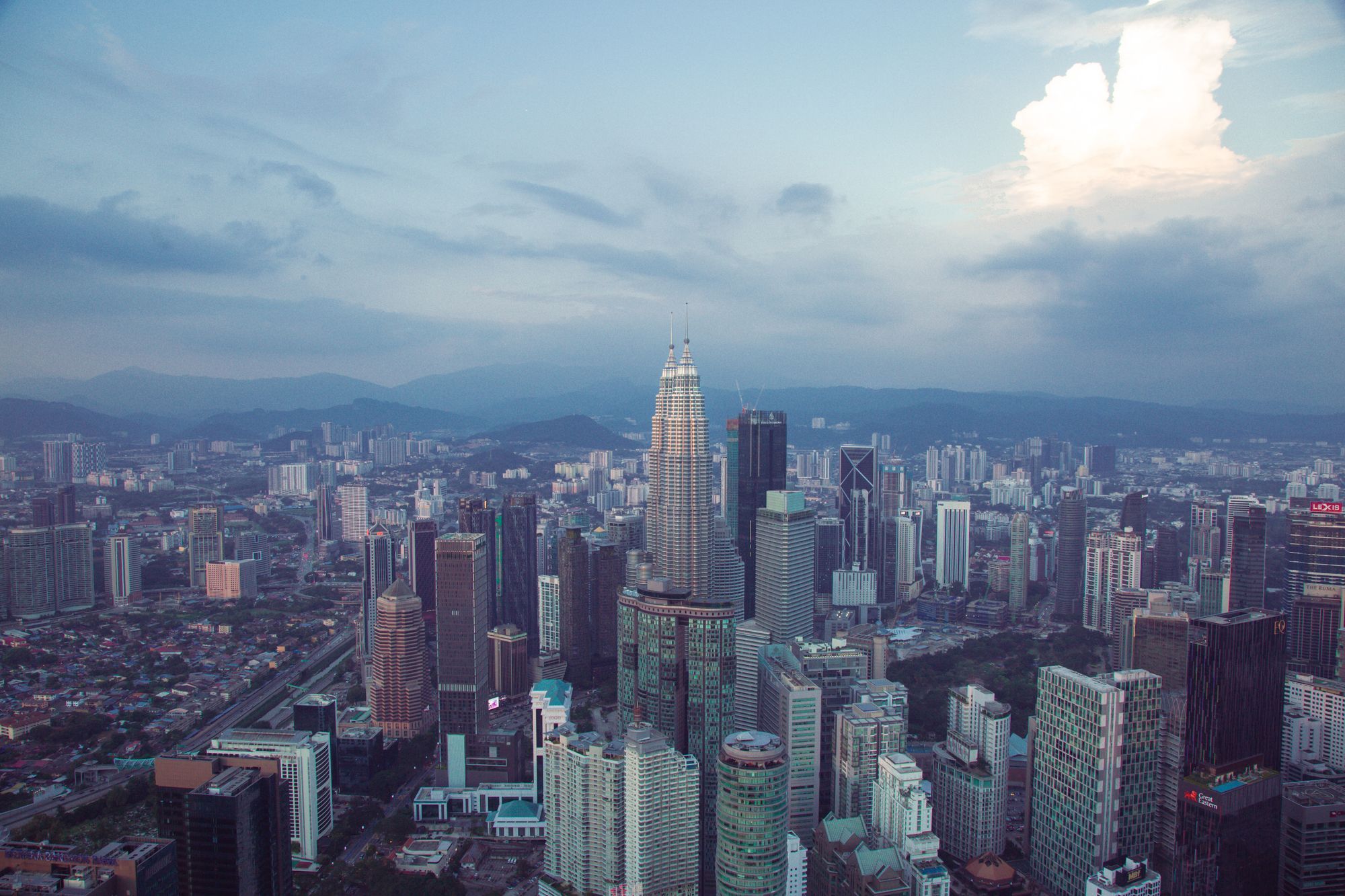 The Kuala Lumpur skyline at sunset with the Petronas Towers in the middle, seen from above.