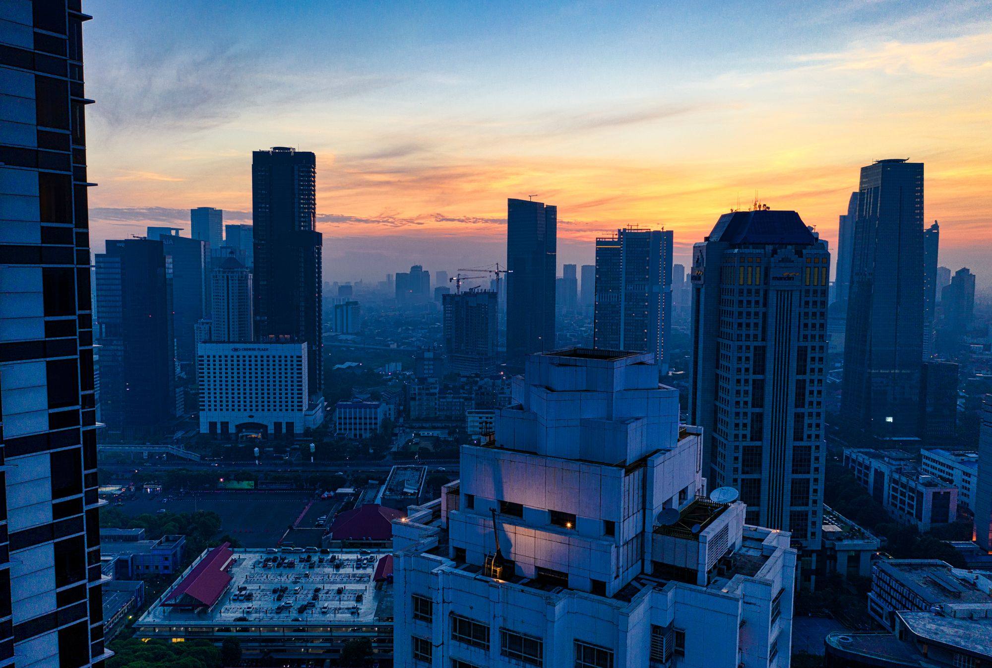 Skyscrapers in central Jakarta at sunset, with an orange sky above and the city in blue shade below.