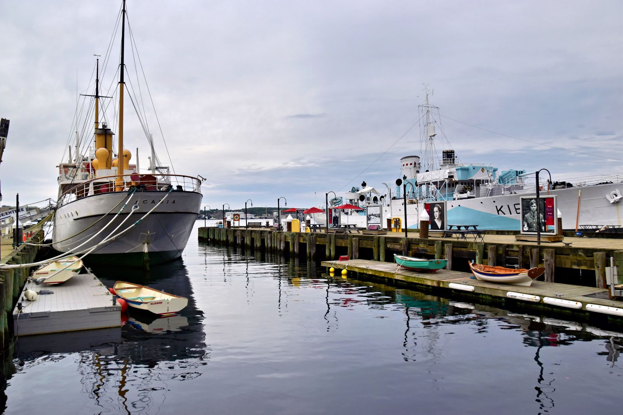 Historic ships moored at the Halifax waterfront, with a wooden boardwalk beside the water.
